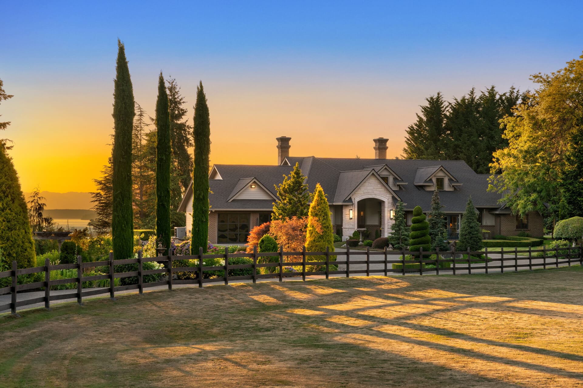 Elegant exterior of a luxury home surrounded by manicured gardens and tall trees at sunset, showcasing a tranquil Pacific Northwest setting.
