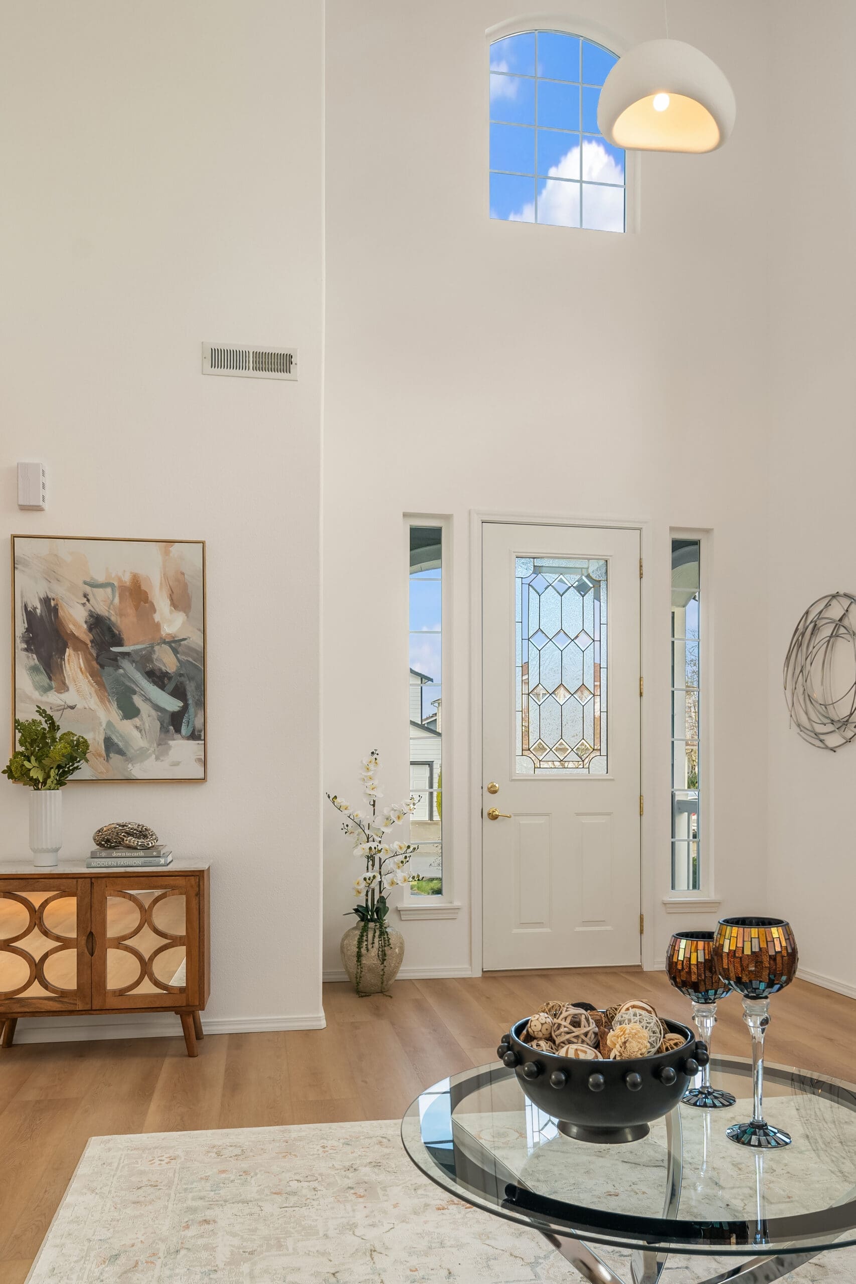 Bright and airy entryway featuring modern design elements, including a decorative console table, stylish artwork, and elegant glass door. Located in the Pacific Northwest, this space exudes a welcoming atmosphere with natural light flooding in through large windows.
