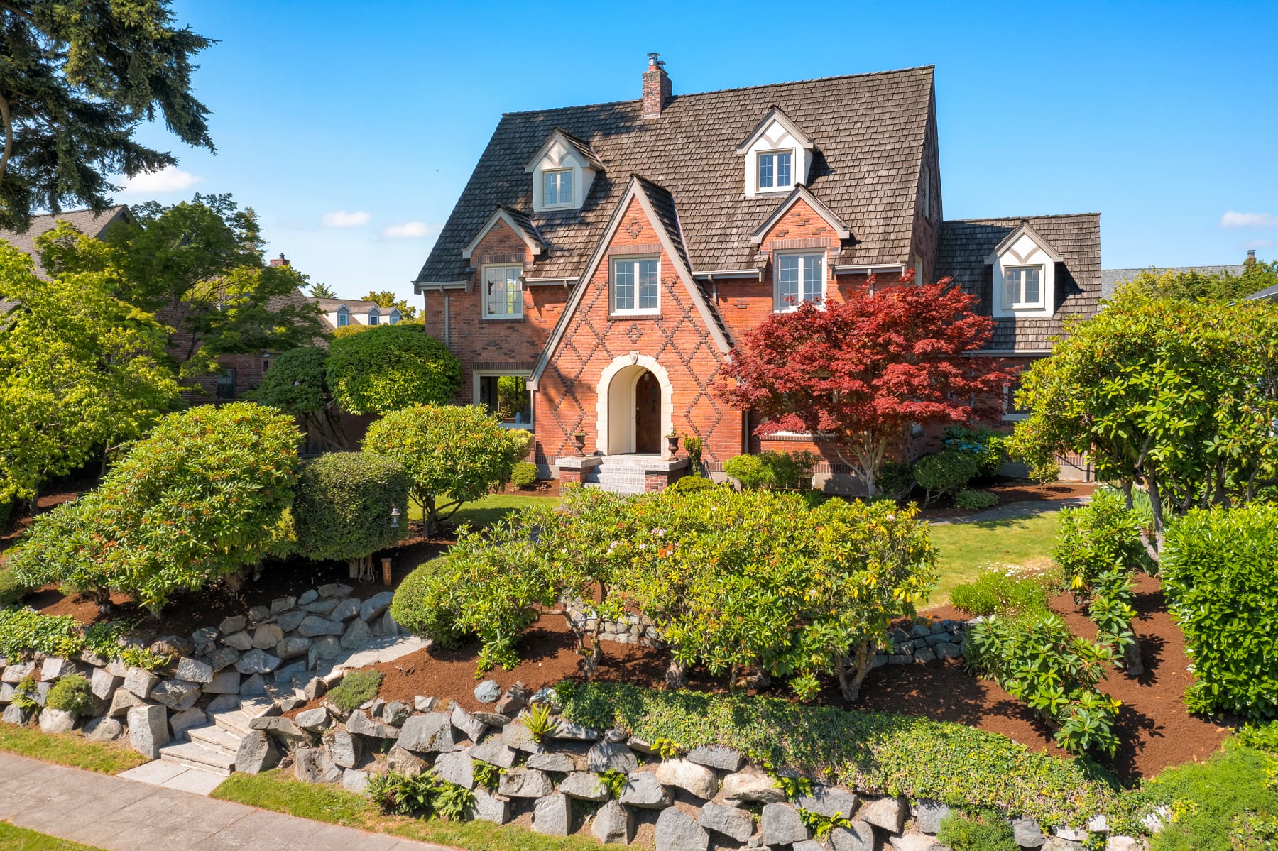 Charming brick exterior of a traditional home surrounded by lush landscaping in the Pacific Northwest, showcasing a welcoming entryway and a vibrant red maple tree.
