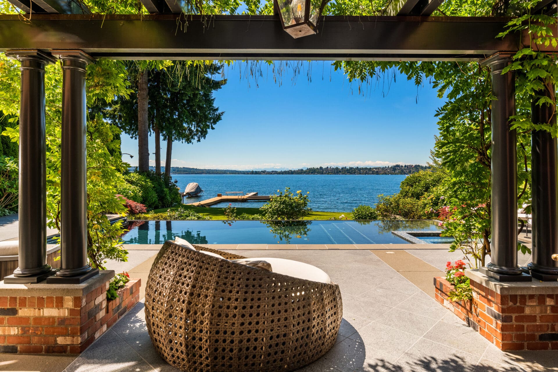 Elegant outdoor living space with a cozy woven chair, overlooking a stunning waterfront view in the Pacific Northwest. Features a serene pool and lush greenery, perfect for relaxation.