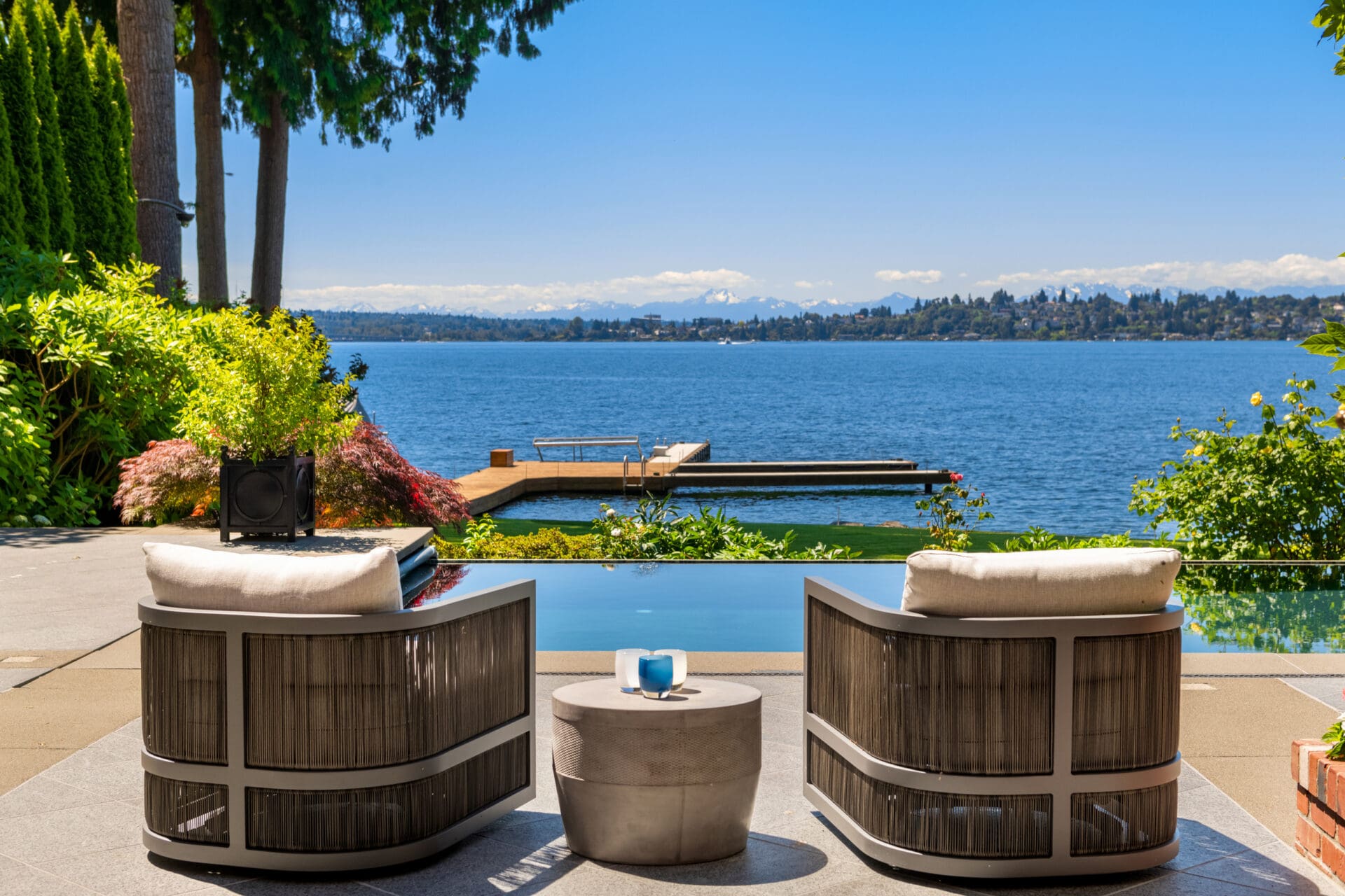 Modern outdoor lounge area with stylish seating and a serene view of a lake, surrounded by lush greenery, located in the Pacific Northwest.