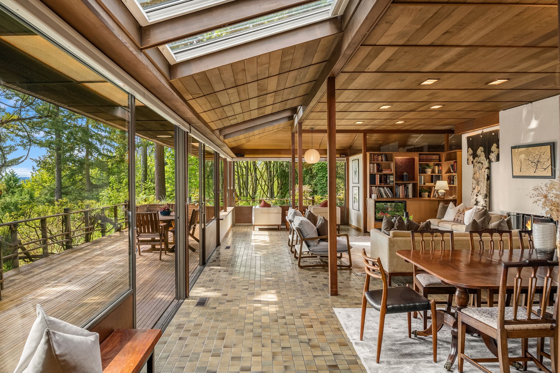 Spacious modern living room with large windows, skylights, and a seamless connection to the outdoor deck, featuring warm wood tones and elegant furnishings, located in the Pacific Northwest.