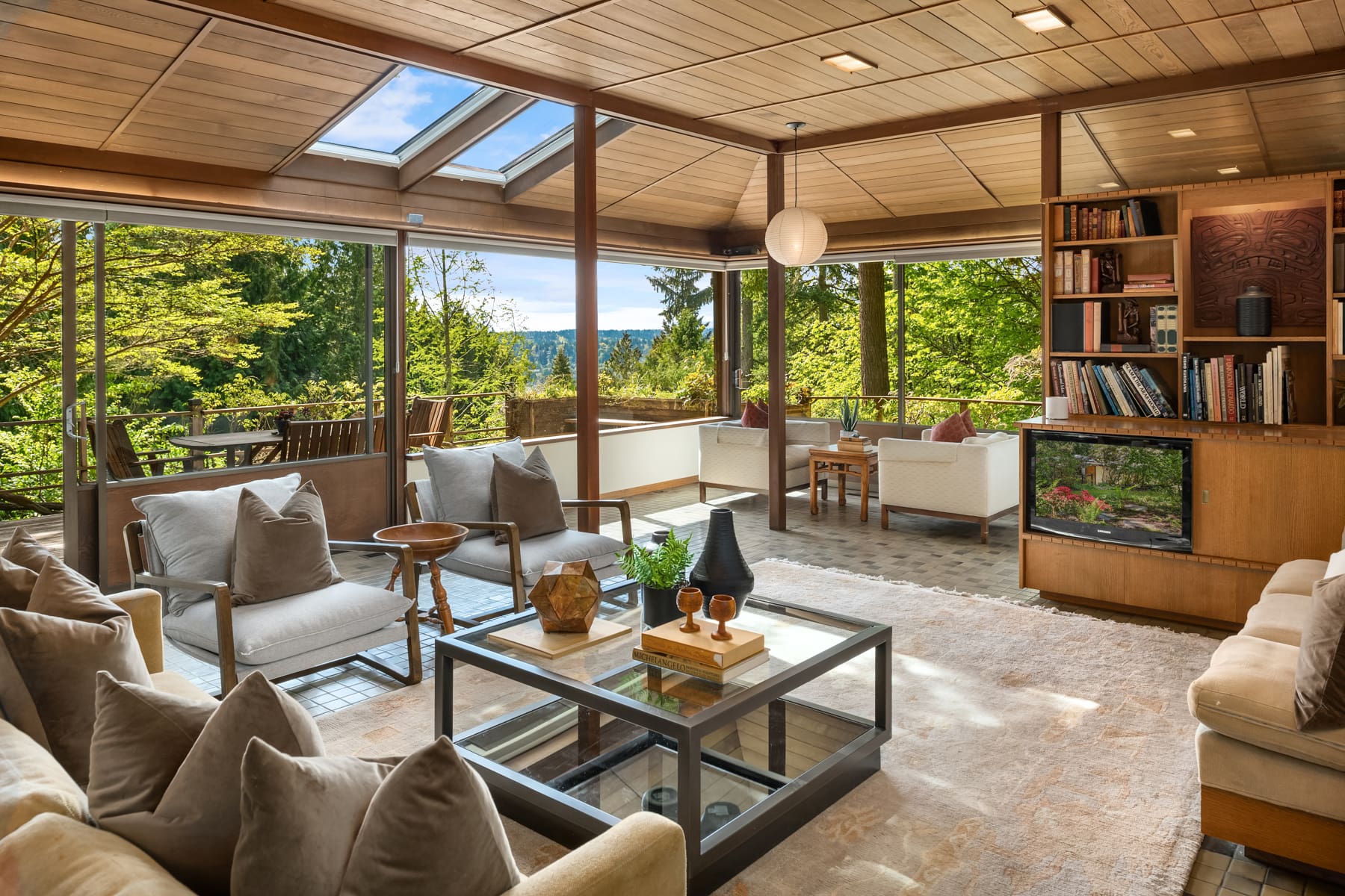 Modern living room with large windows and skylights, featuring cozy seating and a stylish coffee table, surrounded by lush greenery in the Pacific Northwest.
