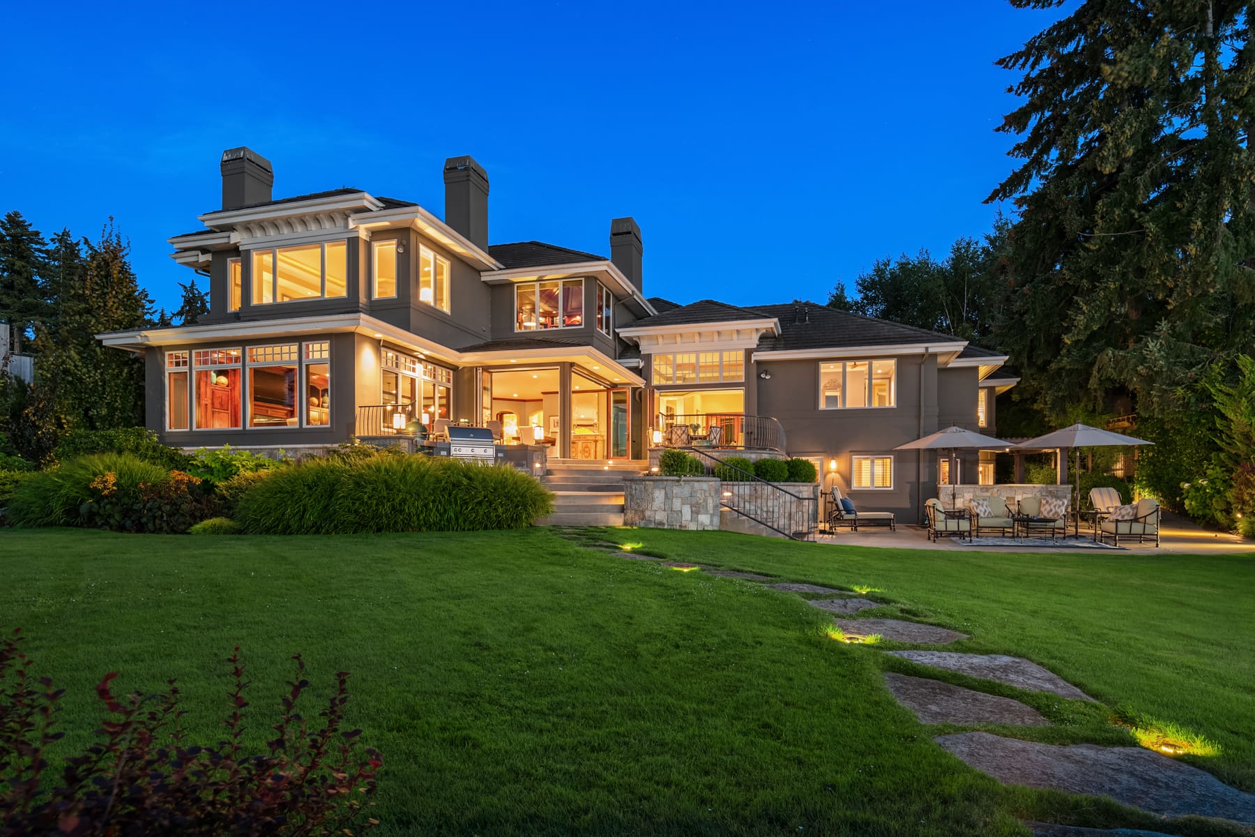Elegant exterior of a modern luxury home in the Pacific Northwest, showcasing beautifully landscaped grounds and warm lighting at twilight.