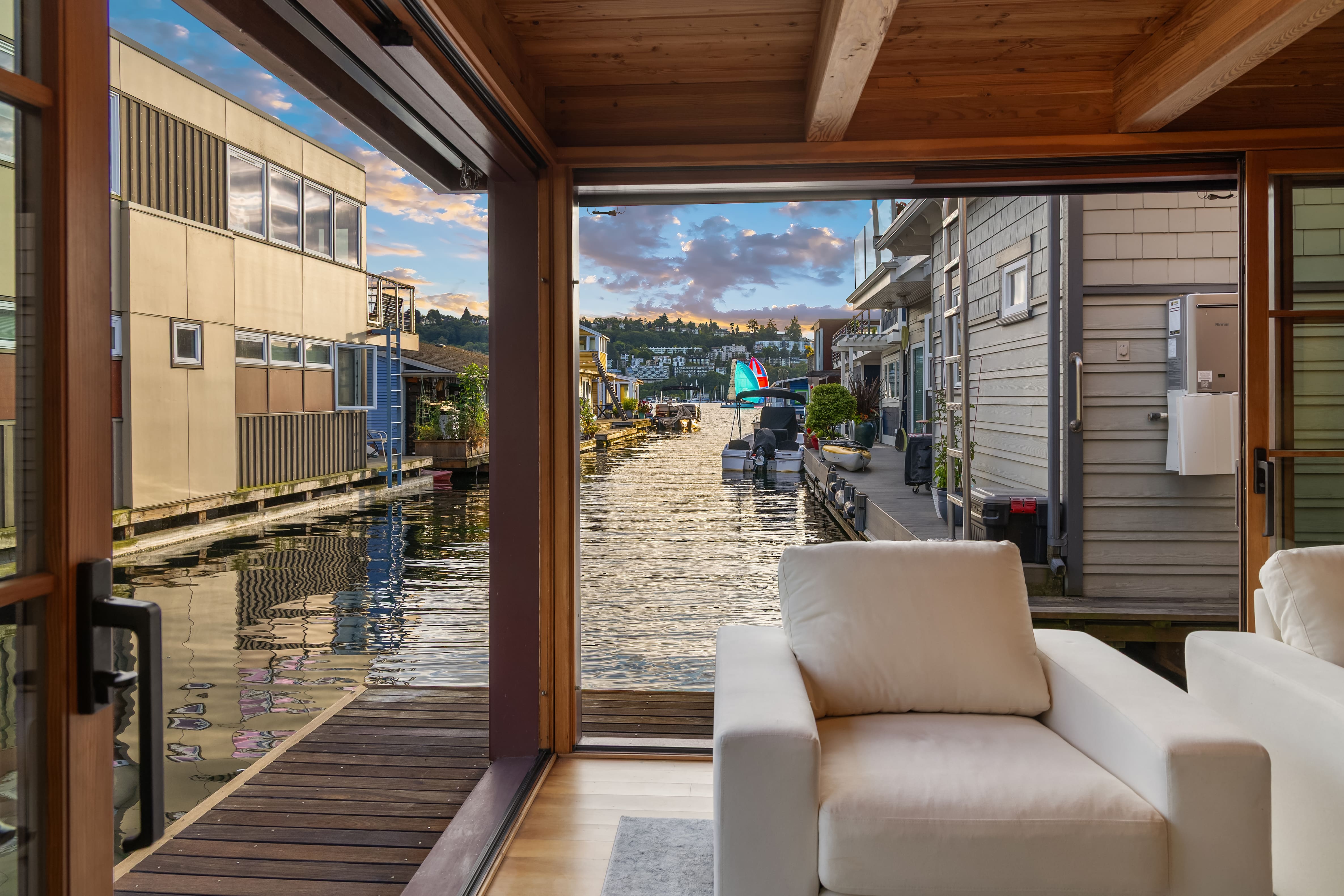 Modern waterfront living room with large windows overlooking a serene canal in Seattle, featuring cozy white seating and a warm, inviting atmosphere.