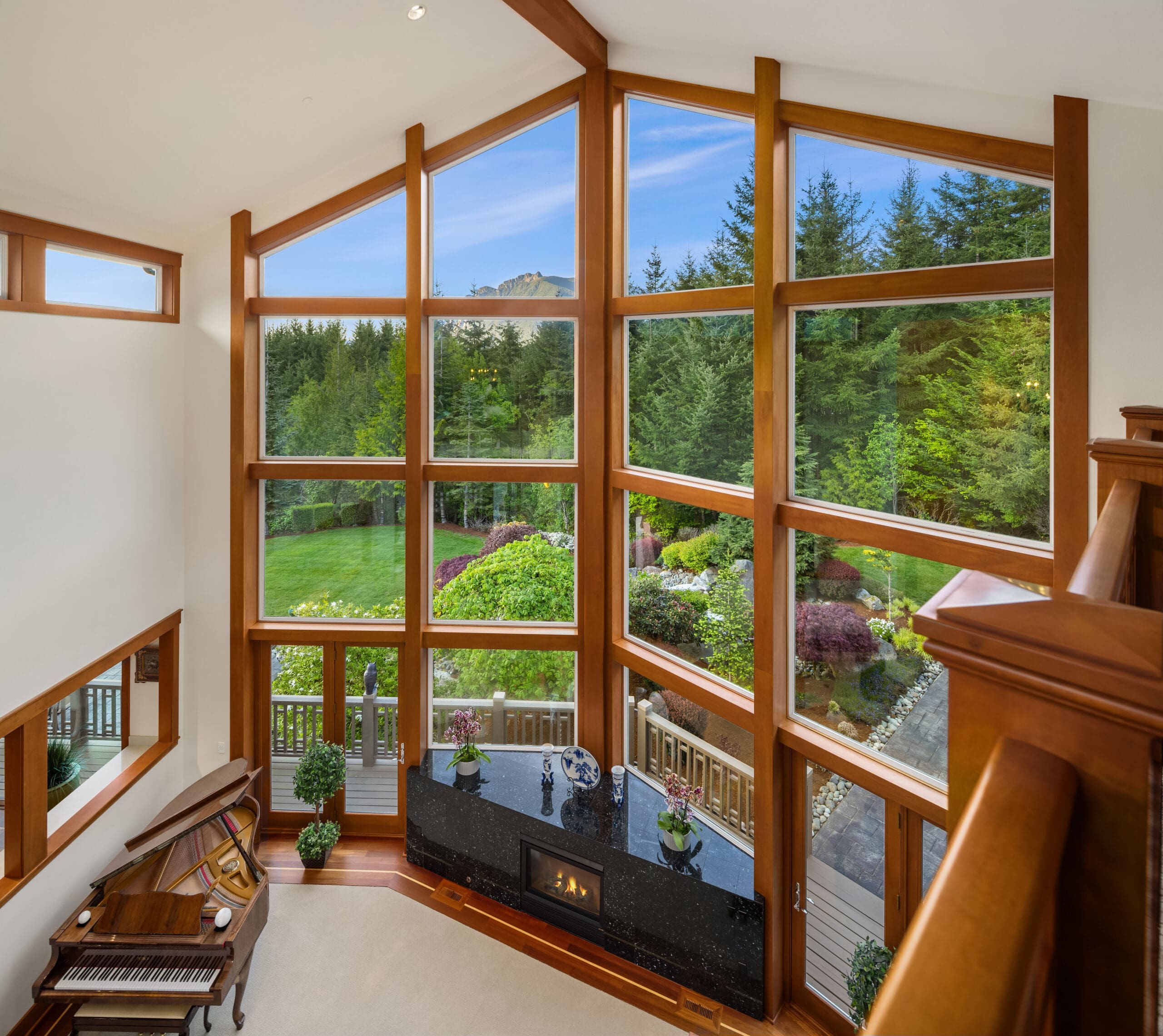 Elegant living room with large windows showcasing lush greenery, featuring wooden accents and a grand piano, located in the Pacific Northwest.
