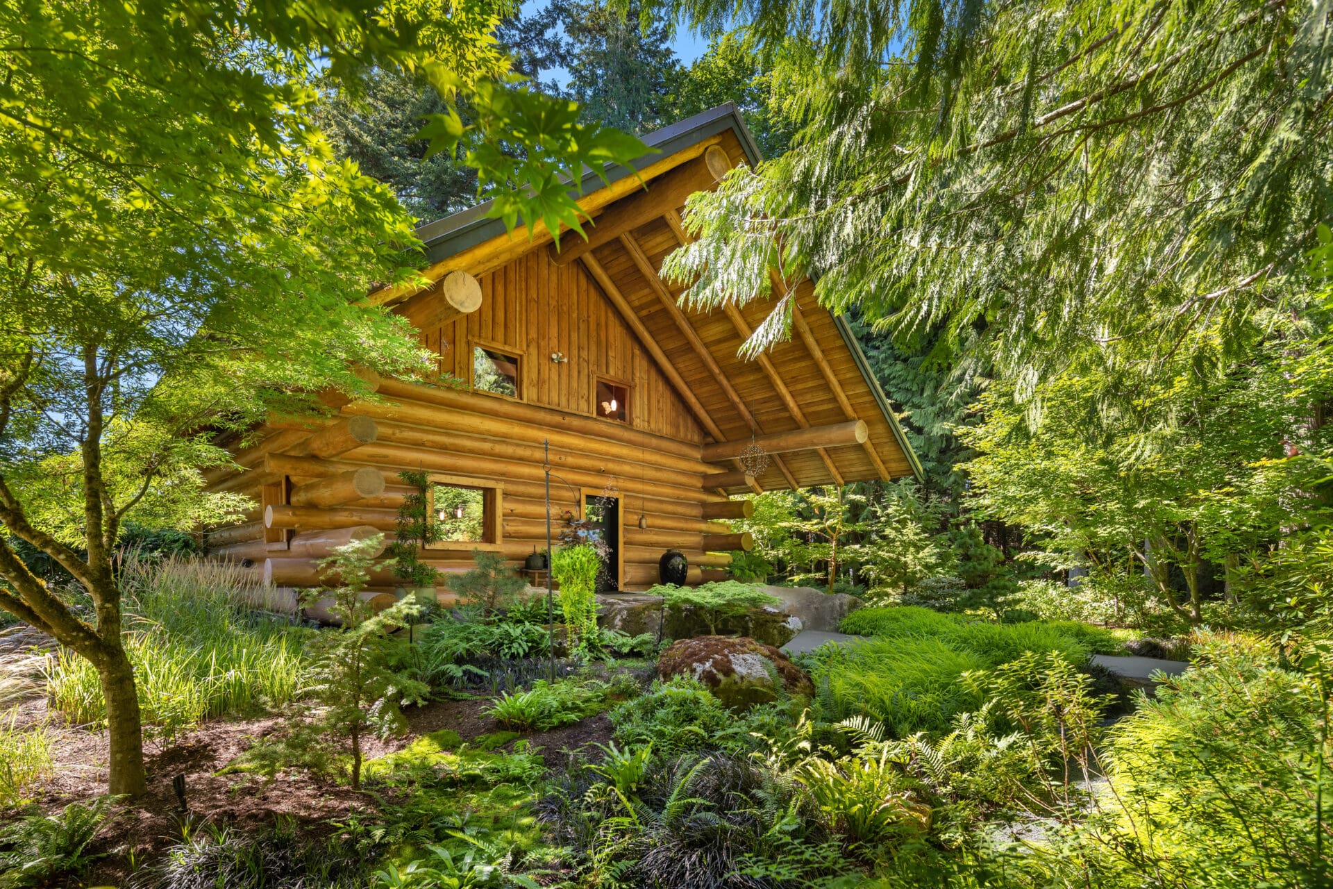 Charming log cabin exterior surrounded by lush greenery in the Pacific Northwest, featuring a sloped roof and large windows that blend seamlessly with the natural landscape.