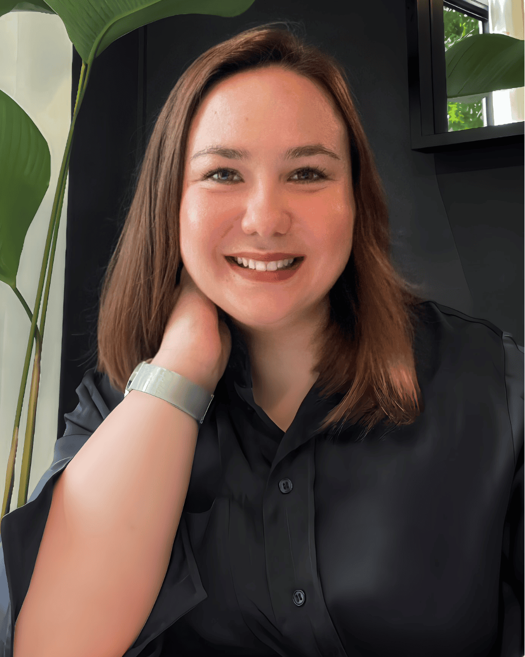 A smiling woman with shoulder-length hair poses in a stylish, modern interior with dark walls and greenery, reflecting an elegant atmosphere typical of Pacific Northwest design.