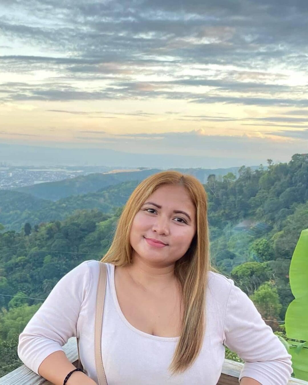 A serene outdoor view showcasing a woman smiling against a backdrop of lush green hills and a colorful sunset, capturing the tranquil beauty of the Pacific Northwest.