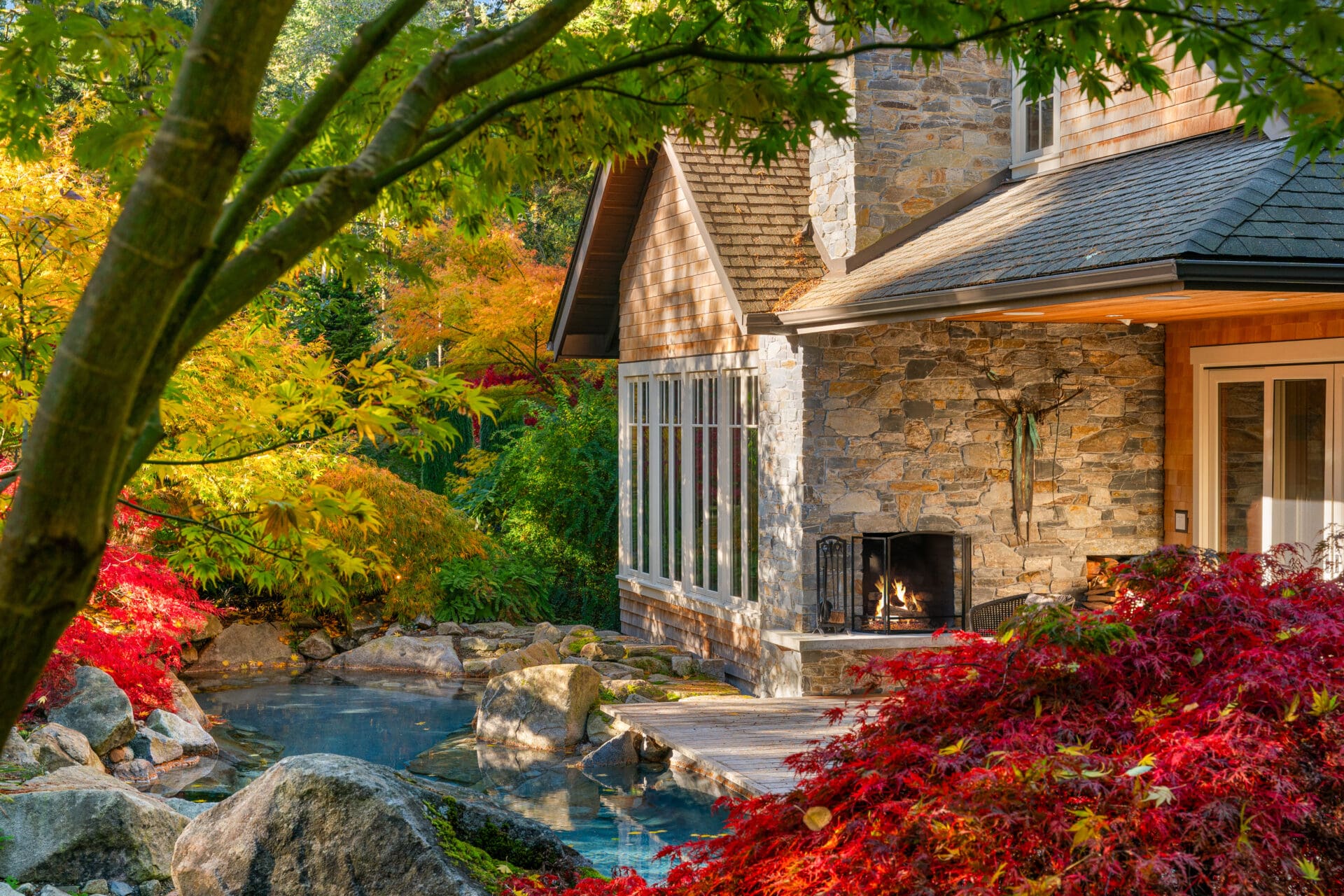 Exterior view of a charming stone house surrounded by vibrant autumn foliage, featuring a cozy outdoor fireplace, located in the Pacific Northwest.
