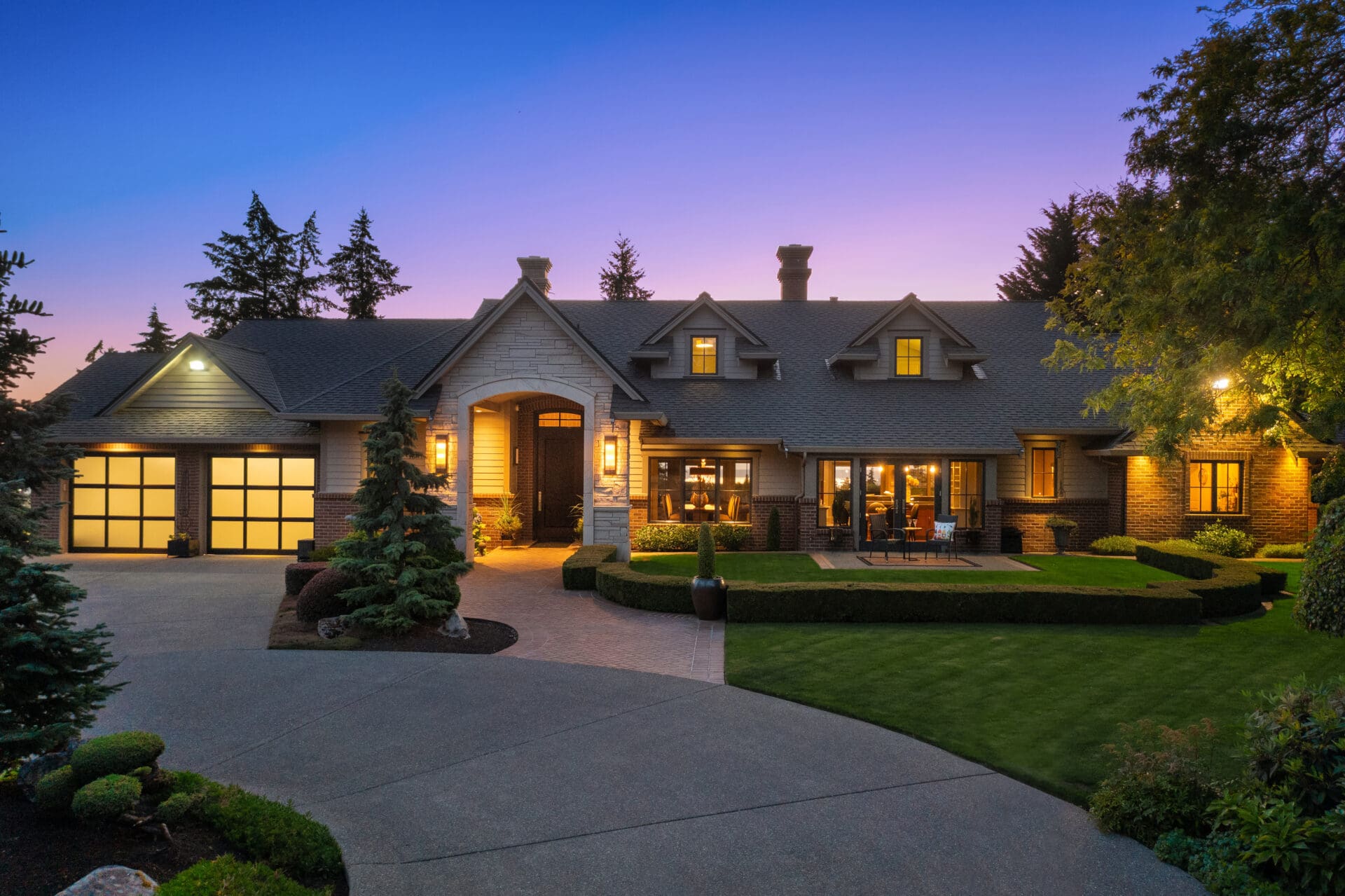 Elegant exterior of a luxury home at twilight in the Pacific Northwest, featuring a beautifully landscaped yard, inviting entrance, and warm lighting illuminating the façade.