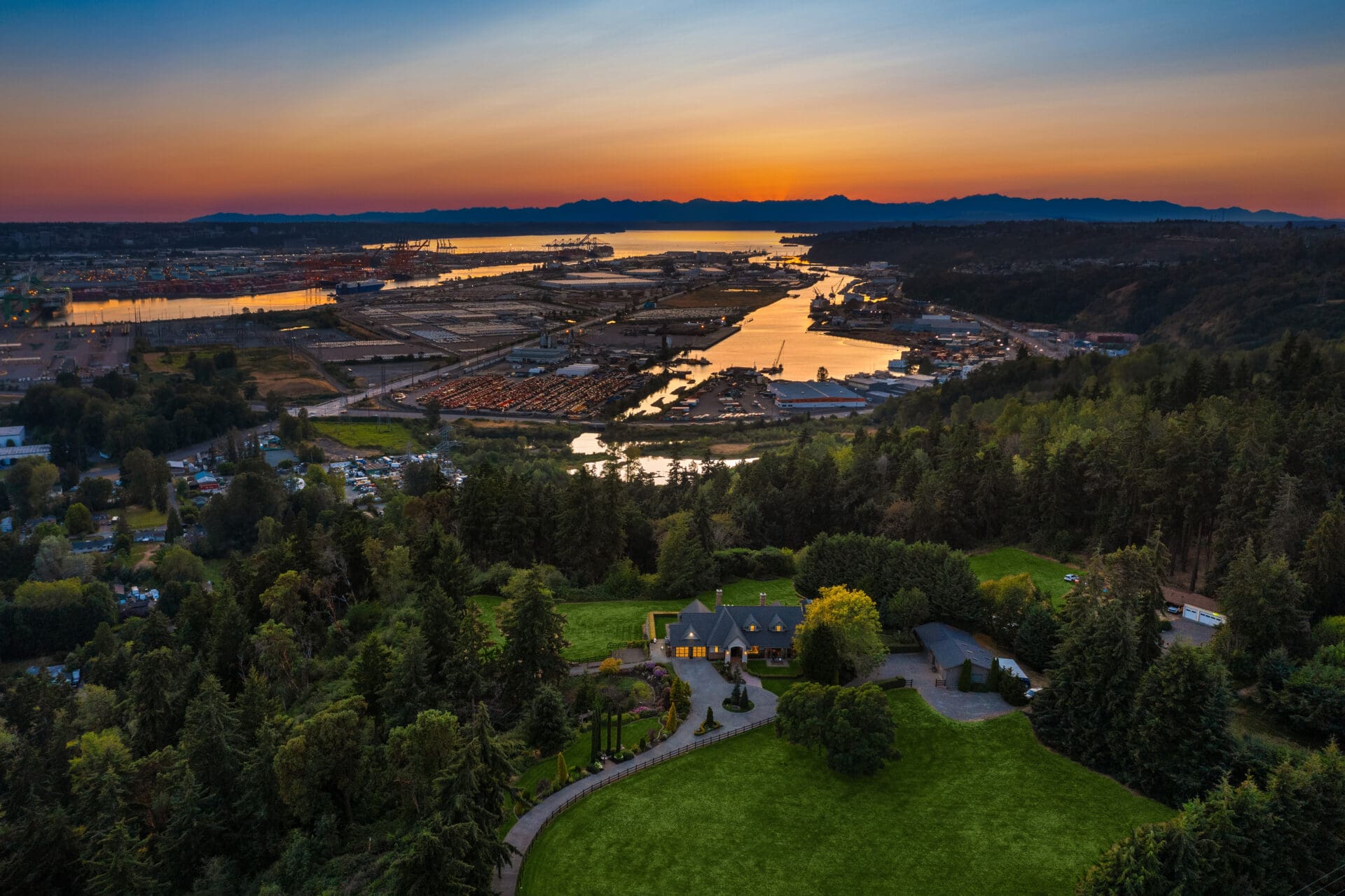 Aerial view of an elegant home surrounded by lush greenery, showcasing a scenic waterfront and sunset in the Pacific Northwest.