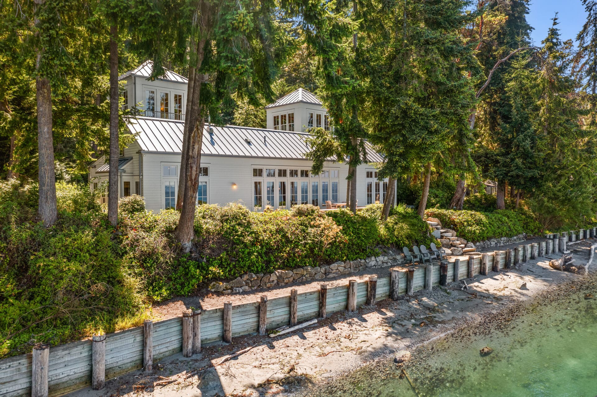 Modern waterfront home surrounded by lush greenery in the Pacific Northwest, featuring large windows and a sleek metal roof, ideal for serene living.