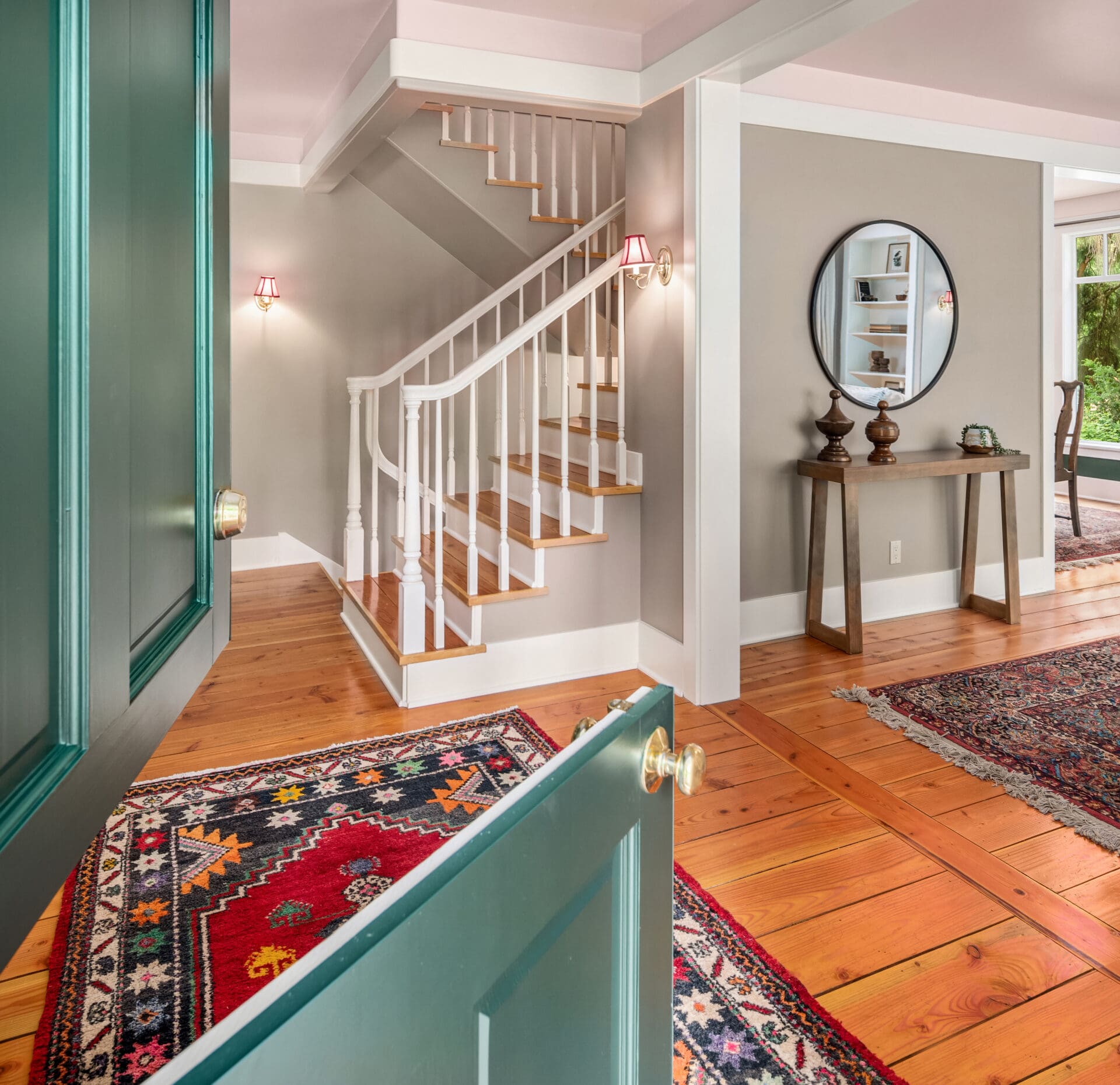Welcoming entryway with a green door, elegant staircase, and hardwood floors, featuring modern decor and warm lighting, located in the Pacific Northwest.