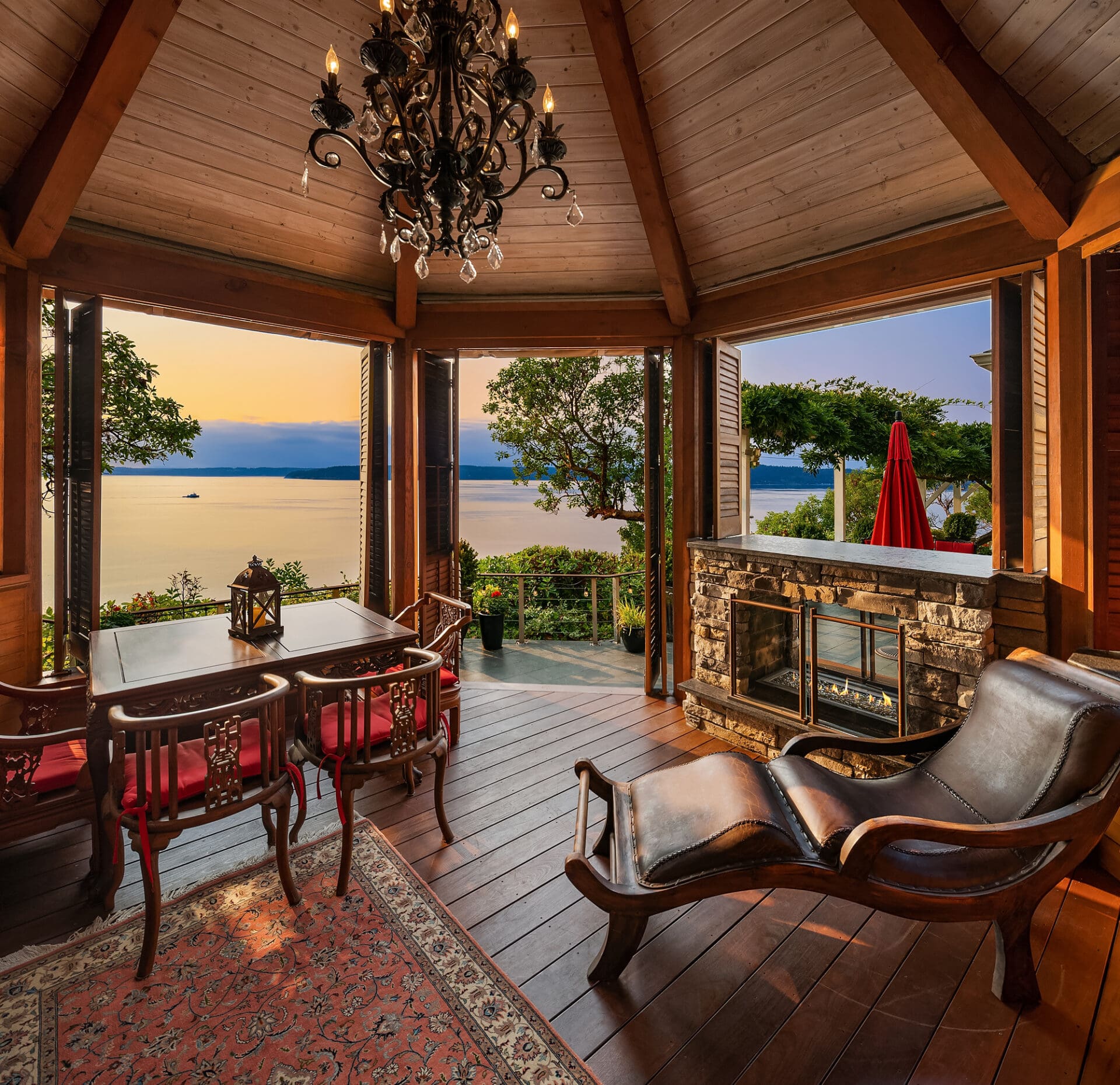 Cozy living room with stunning waterfront views, featuring a wooden ceiling, elegant chandelier, and stone fireplace, set in a serene Pacific Northwest location.