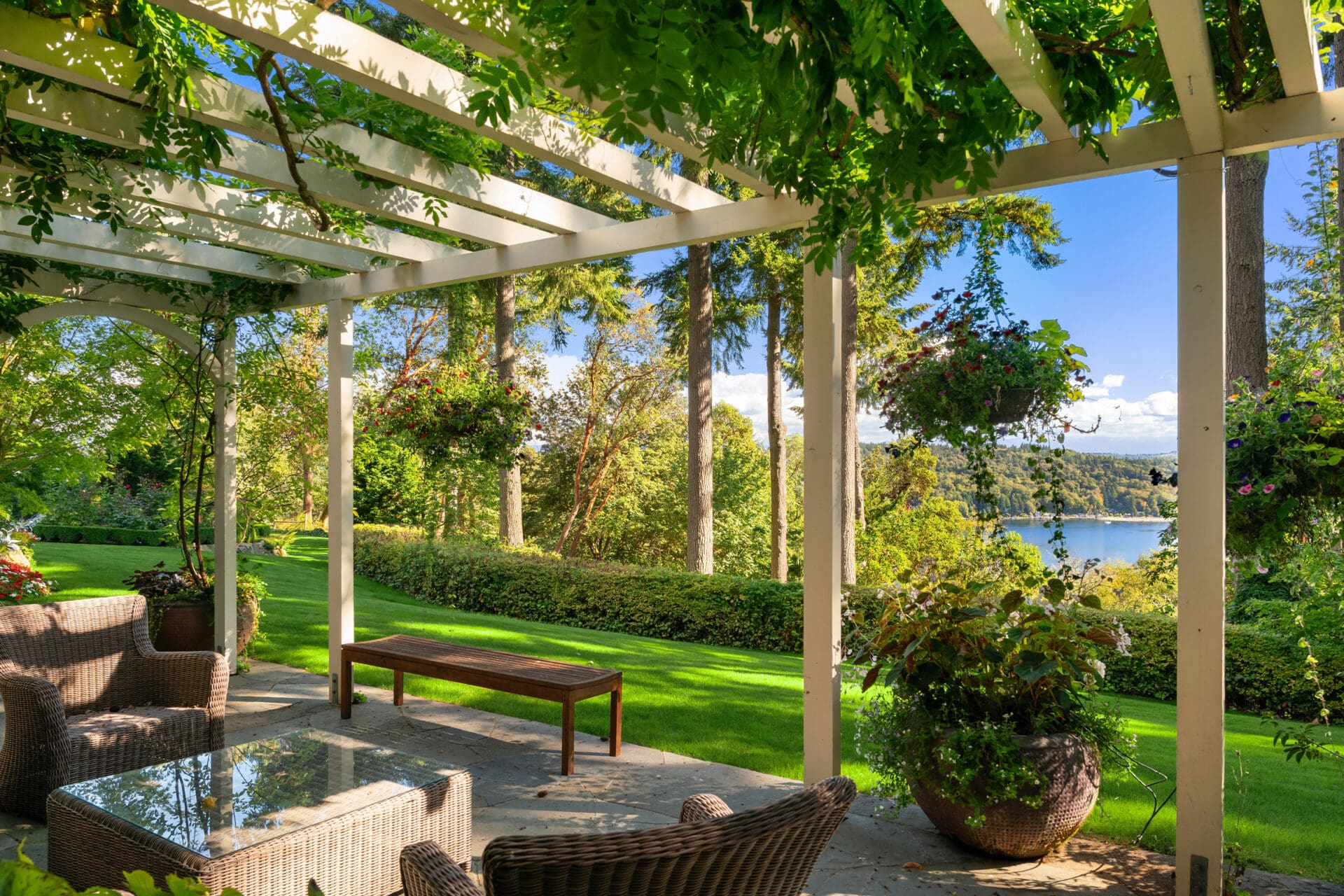 Serene outdoor living space with a covered patio, featuring wicker furniture and lush greenery, overlooking a tranquil lake in the Pacific Northwest.