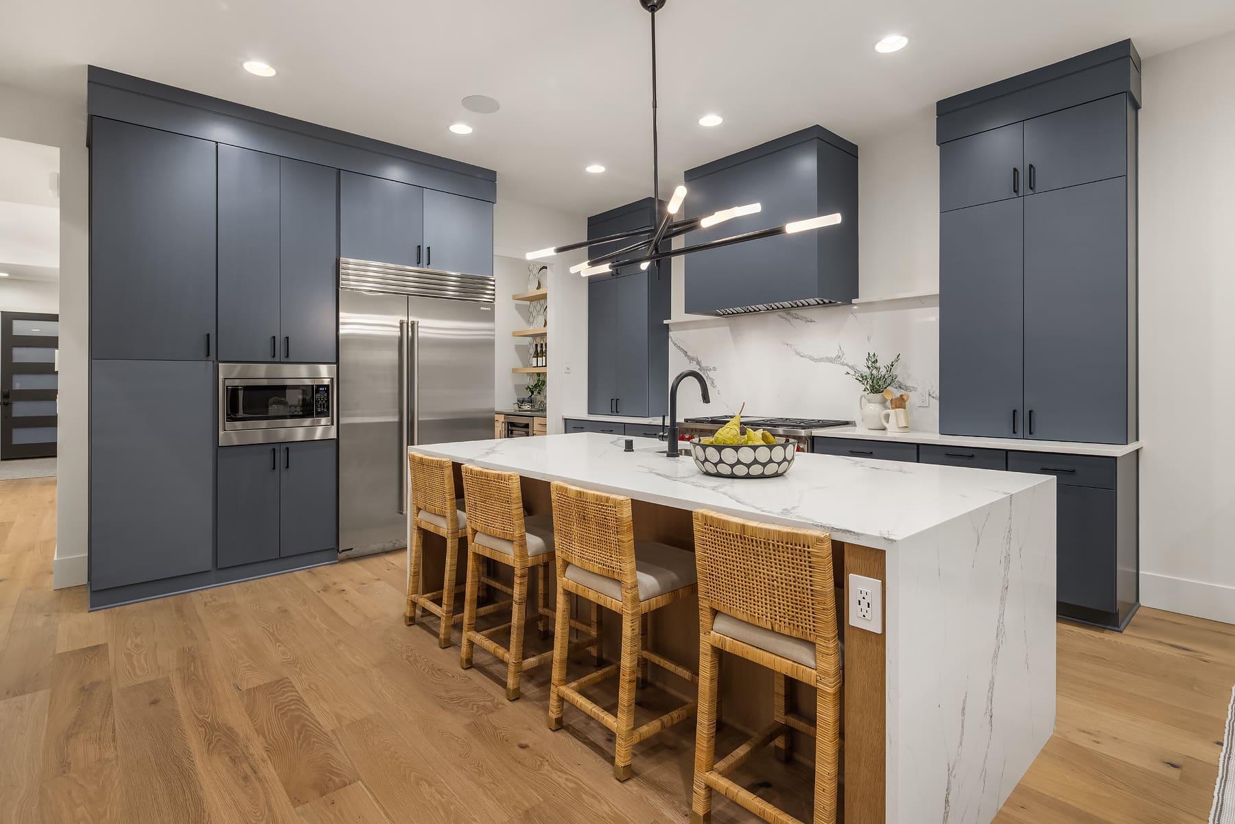 Modern kitchen with navy blue cabinetry, a large marble island, and rattan bar stools, showcasing an elegant design in the Pacific Northwest.