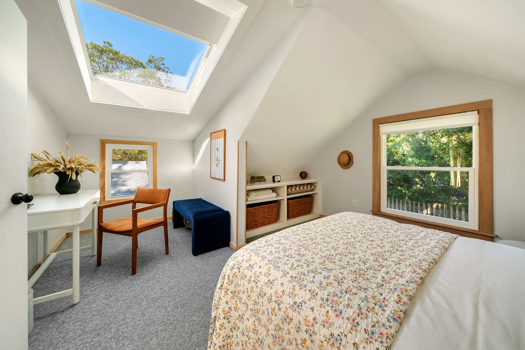 Cozy bedroom with sloped ceilings, featuring a floral-patterned bedspread, skylight, and natural light from windows, located in the Pacific Northwest.