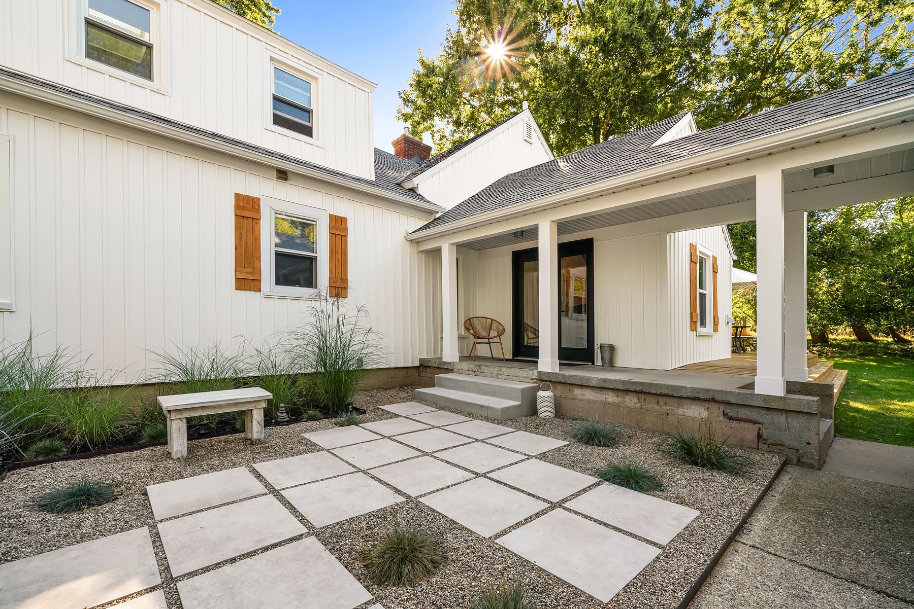 Charming exterior of a modern farmhouse in the Pacific Northwest, featuring a landscaped entryway with stone pavers, decorative wooden shutters, and lush greenery under a bright blue sky.