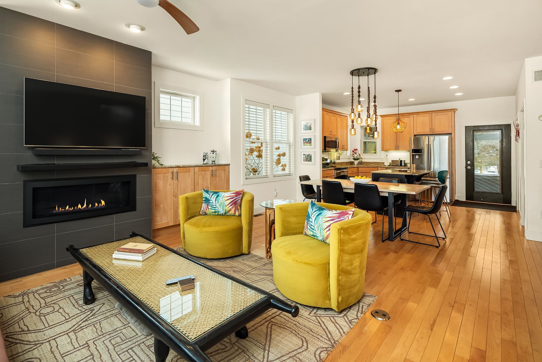 Modern living room with yellow accent chairs, a sleek fireplace, and an open kitchen design, featuring warm wood tones and stylish lighting in a Pacific Northwest home.
