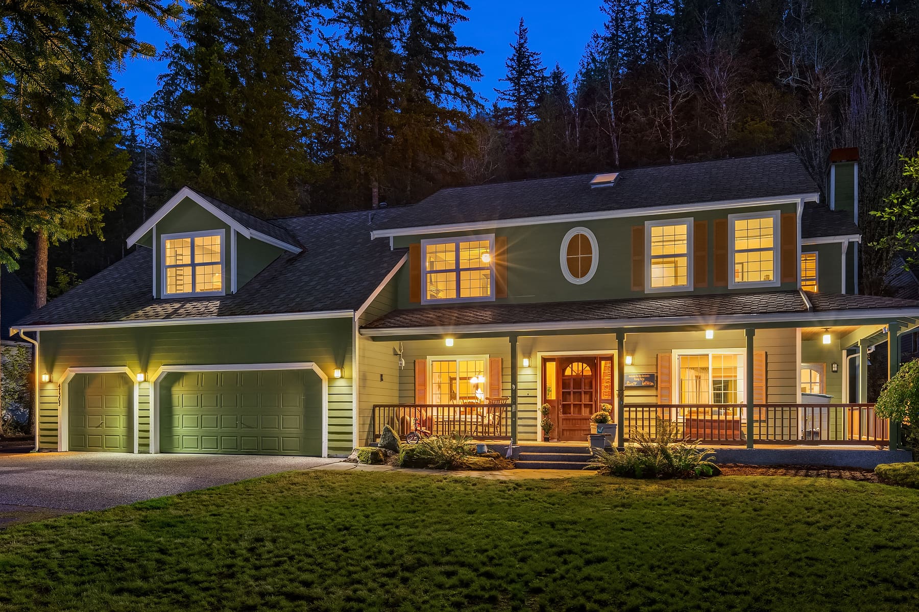 Elegant exterior of a modern green house at twilight, showcasing warm lighting and inviting entryway, located in the Pacific Northwest.