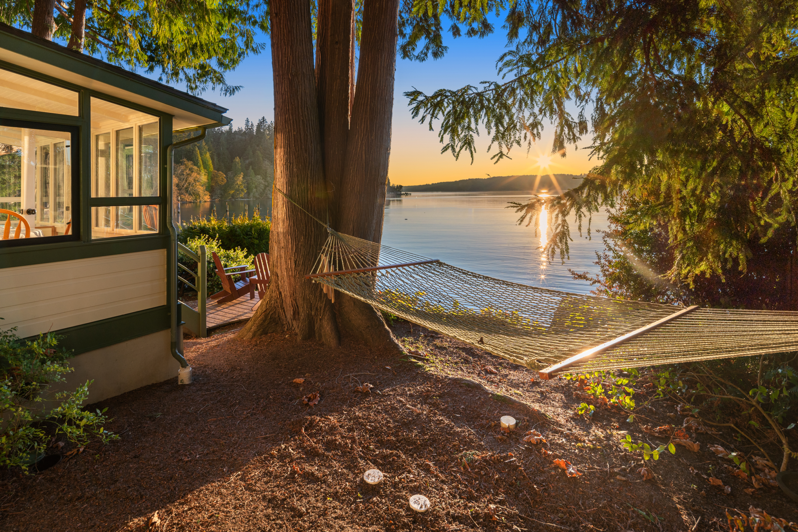 Charming waterfront property in the Pacific Northwest featuring a cozy outdoor hammock nestled between trees, with a serene lake view and sunset glow, ideal for relaxation and leisure.