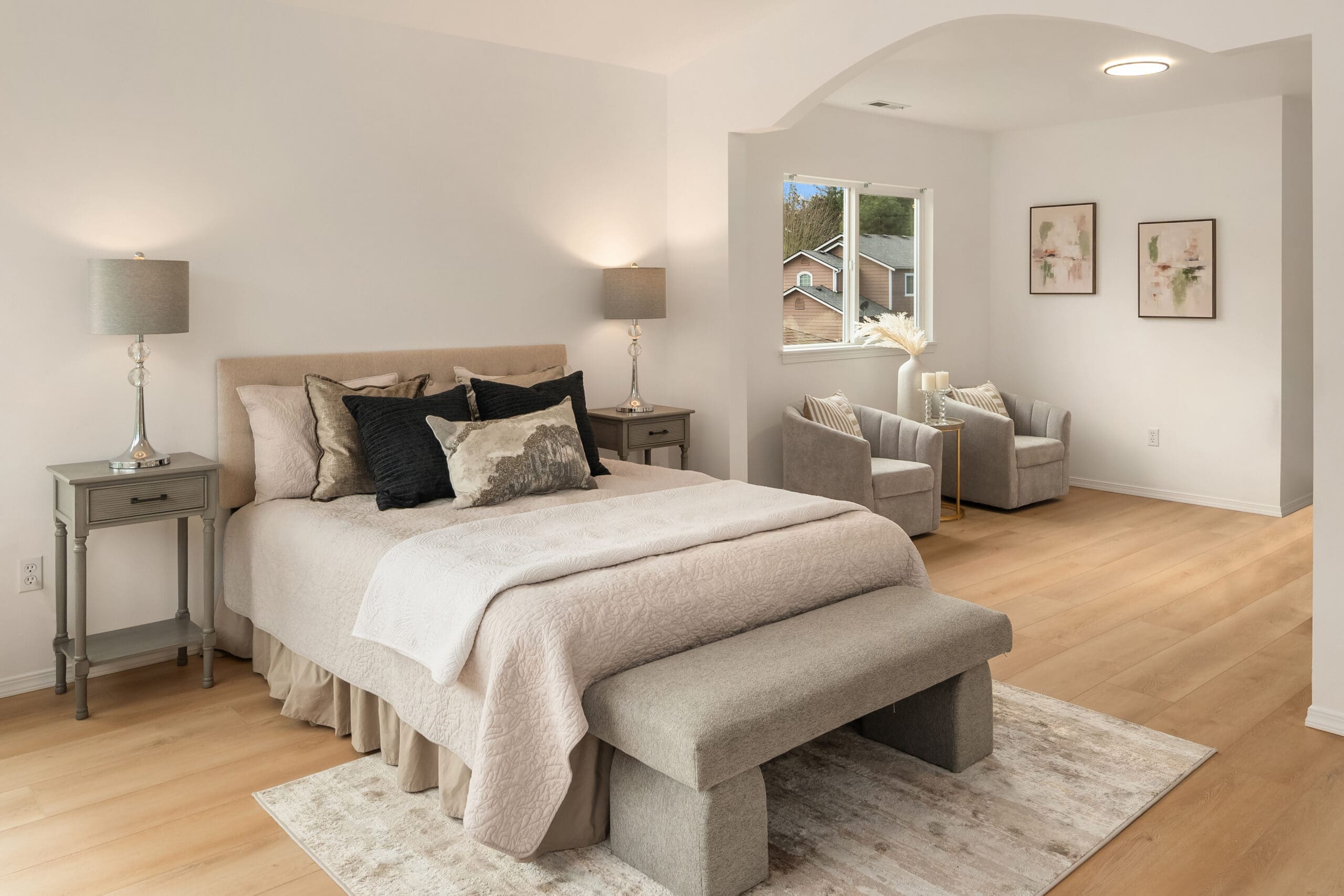 Spacious and modern bedroom featuring a cozy bed with decorative pillows, soft lighting from bedside lamps, and a comfortable seating area. The room showcases elegant wood flooring and neutral tones, creating a serene atmosphere. Located in the Pacific Northwest.