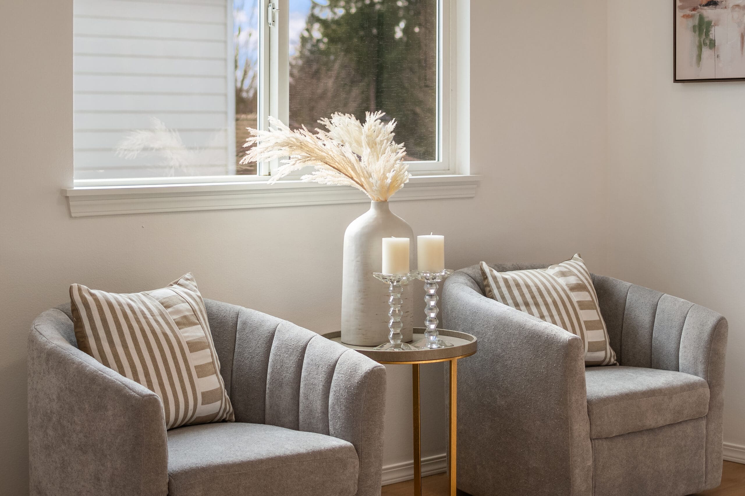 Cozy living room corner in Seattle featuring modern gray armchairs, decorative striped pillows, a chic side table with candles, and a stylish vase with pampas grass, creating an inviting atmosphere.