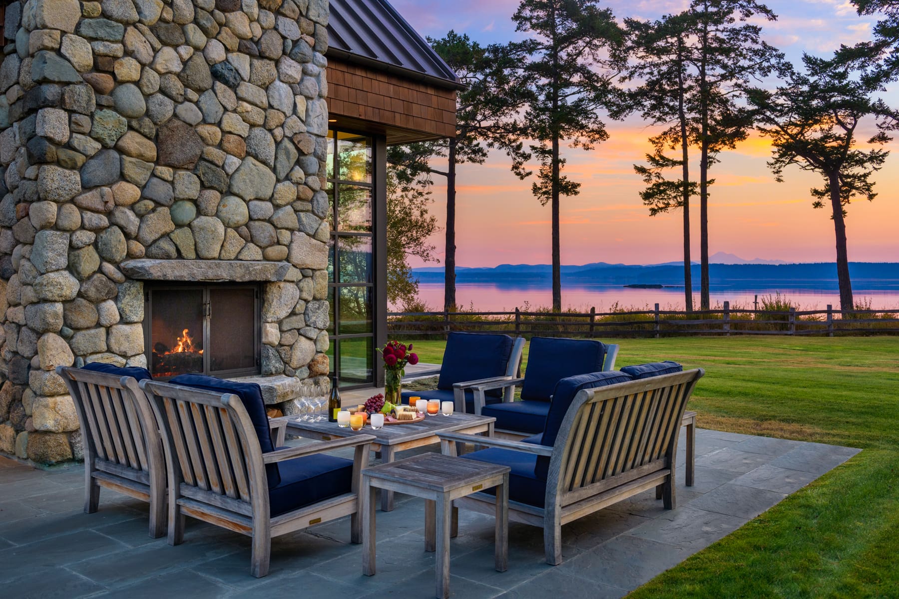 Outdoor living space with stone fireplace and comfortable seating, featuring a modern design and serene sunset view over the water, located in the Pacific Northwest.