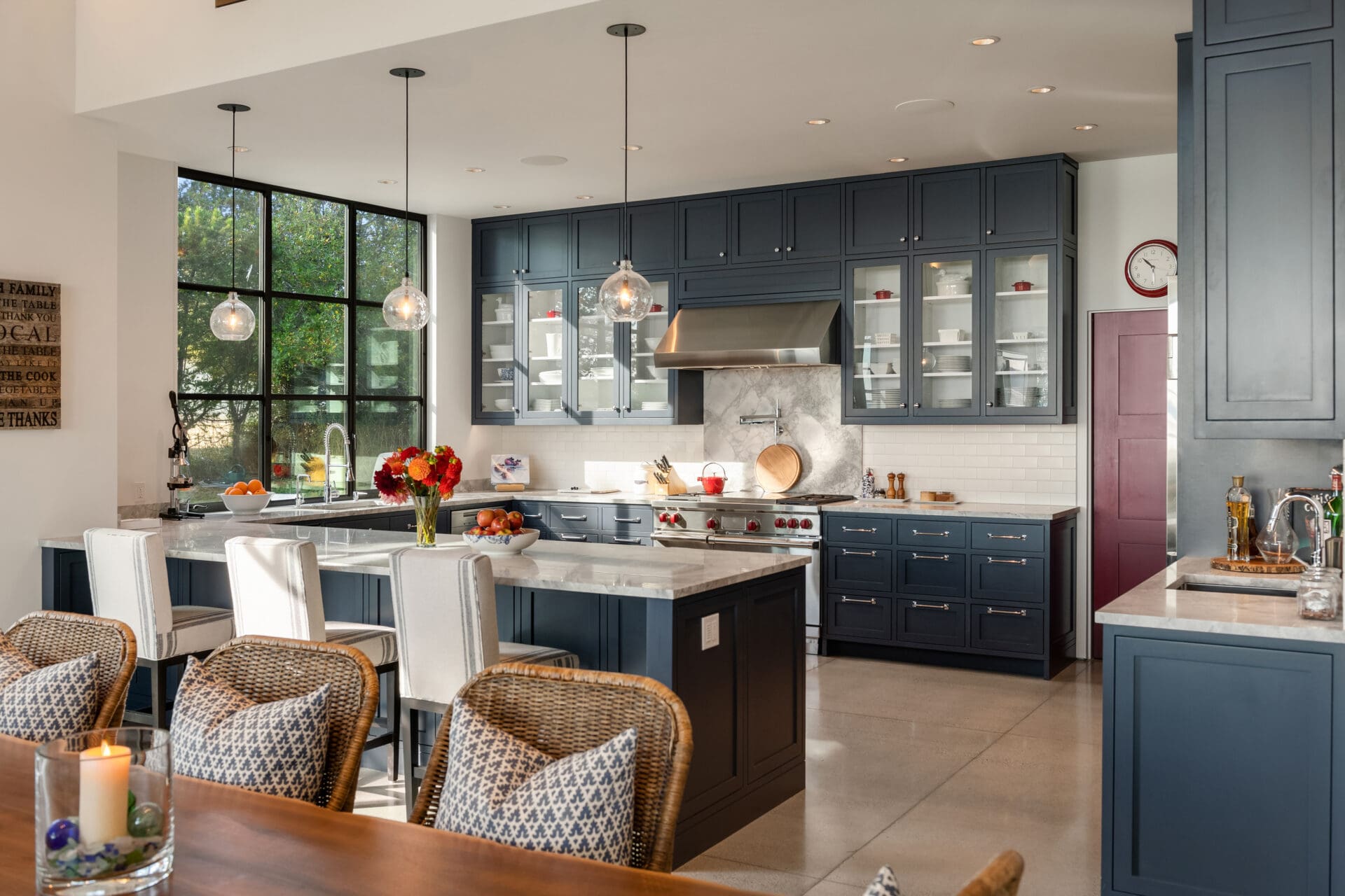 Modern kitchen with navy blue cabinetry, marble countertops, and large windows, featuring elegant pendant lighting. Located in the Pacific Northwest.