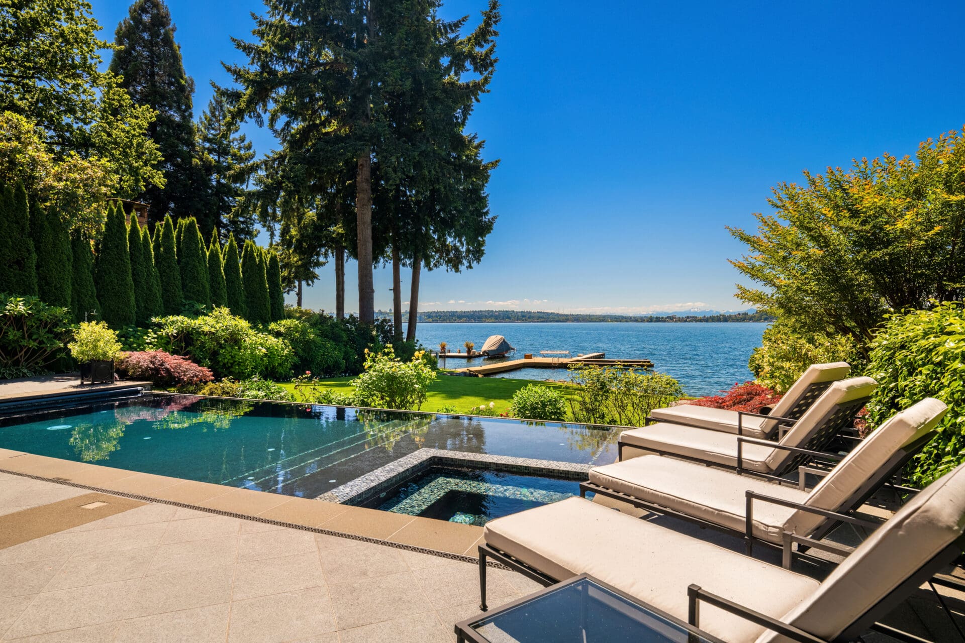 Luxurious outdoor living space featuring a sleek infinity pool and comfortable lounge chairs, surrounded by lush greenery and a stunning view of the water, in the Pacific Northwest.