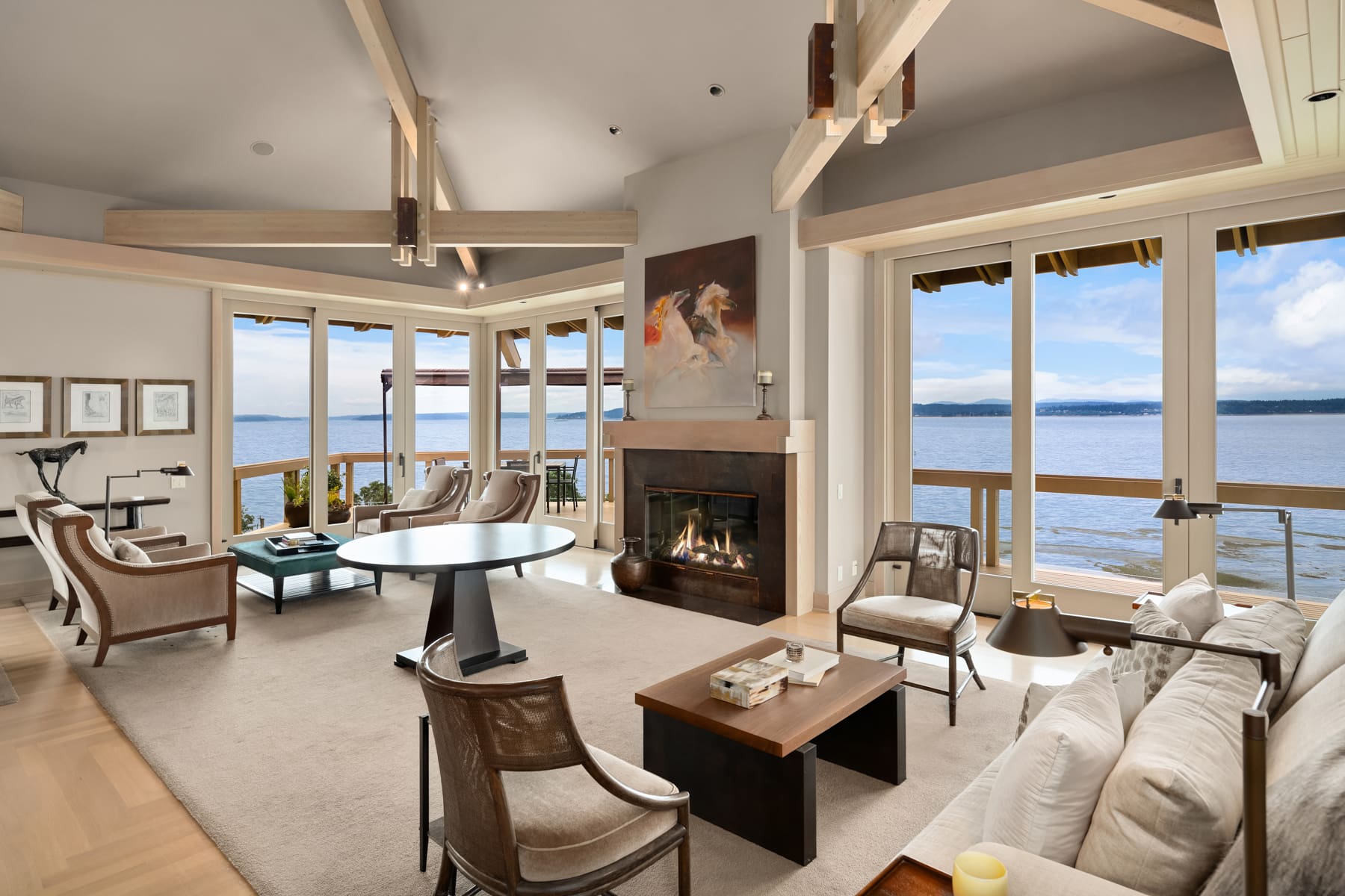 Modern waterfront living room with large windows offering stunning views of the water, featuring elegant furnishings and a cozy fireplace, located in the Pacific Northwest.
