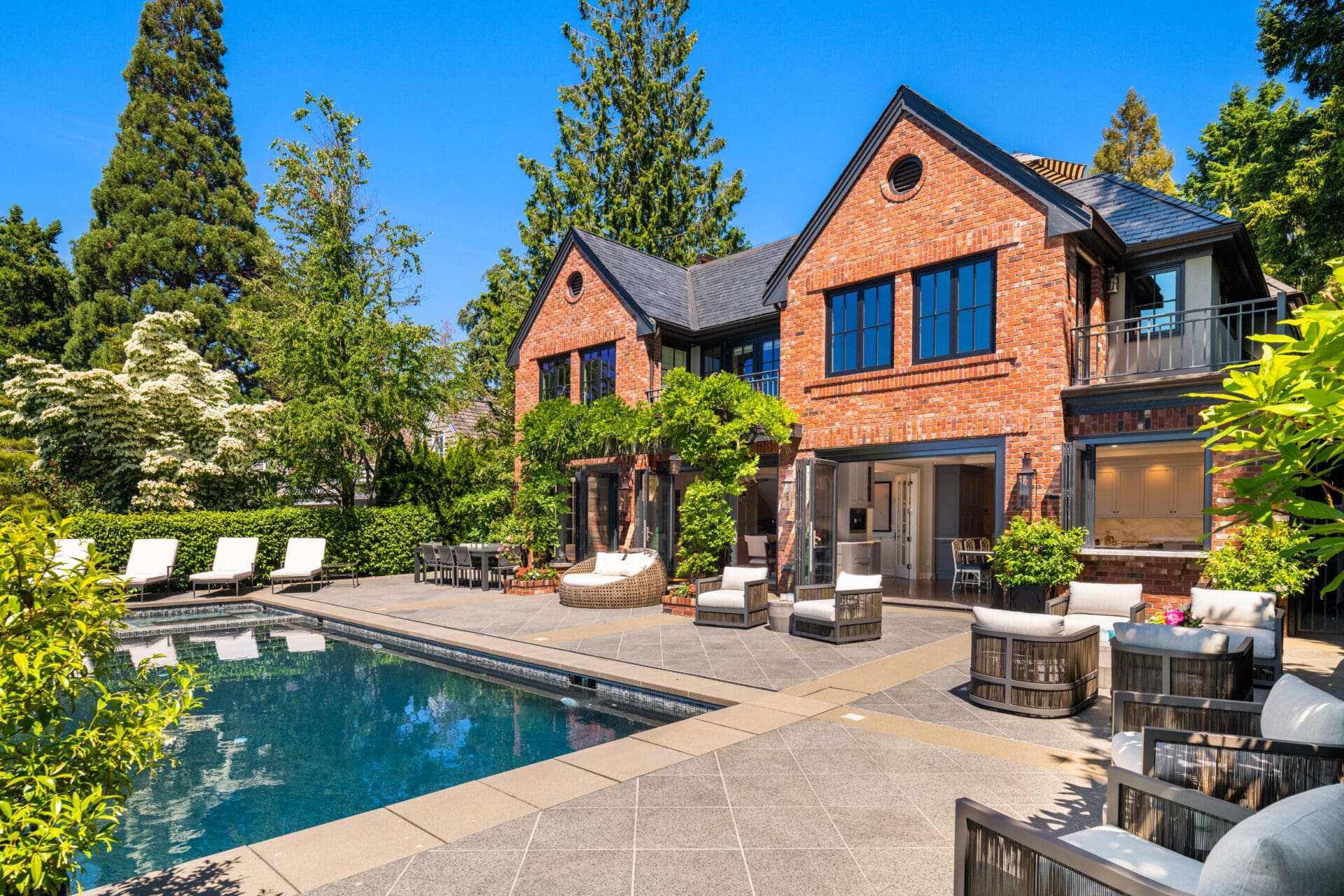 Elegant outdoor living space featuring a luxurious pool, stylish lounge chairs, and lush greenery, set against a beautiful brick home in the Pacific Northwest.