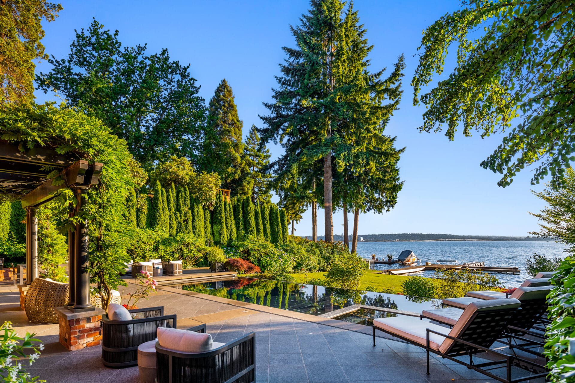 Stunning outdoor living space featuring a serene waterfront view in the Pacific Northwest, with lush greenery, a sleek pool, and stylish seating areas, perfect for relaxation and entertaining.