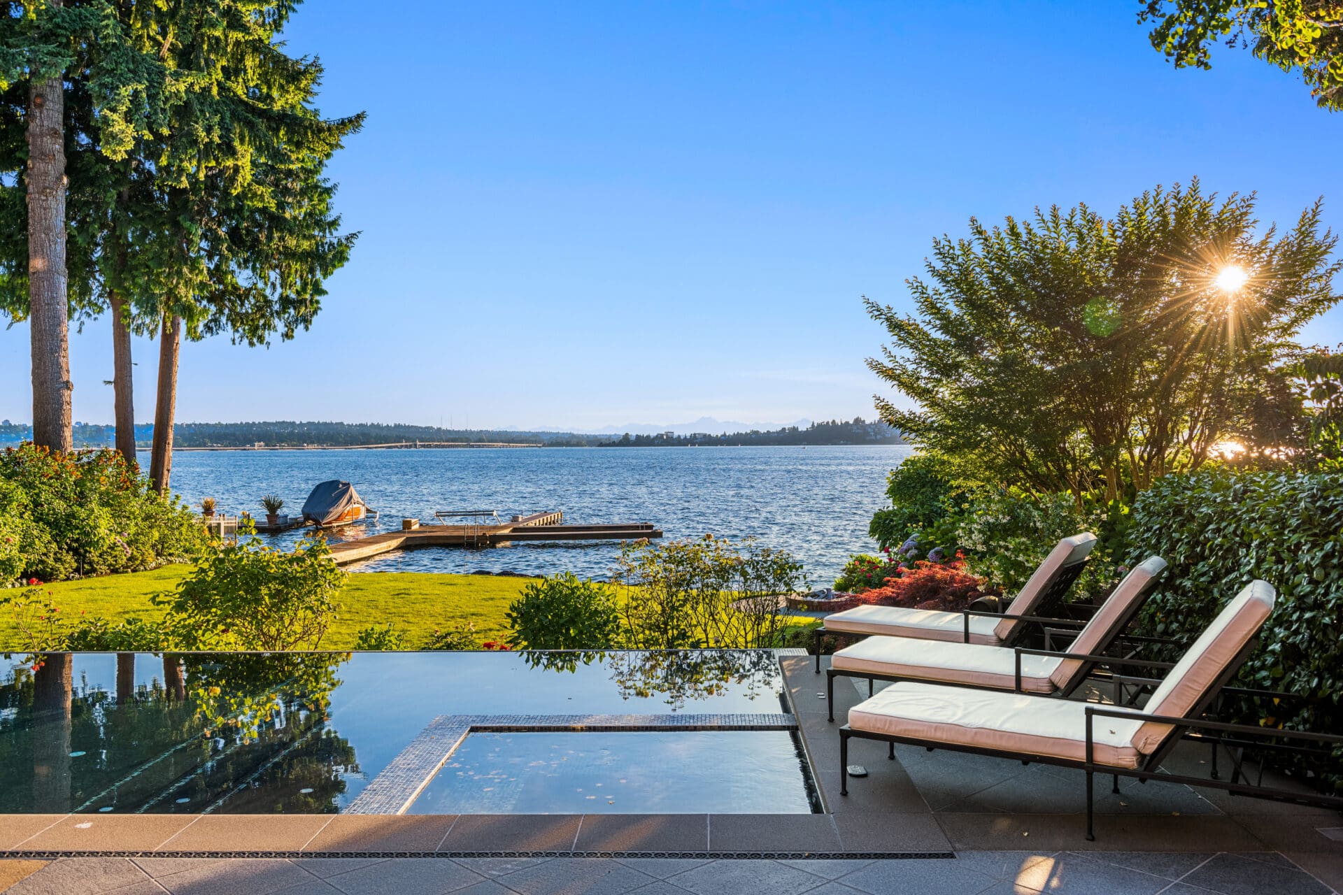 Stunning waterfront view from a luxurious outdoor space featuring a sleek infinity pool, comfortable lounge chairs, and lush landscaping in the Pacific Northwest.