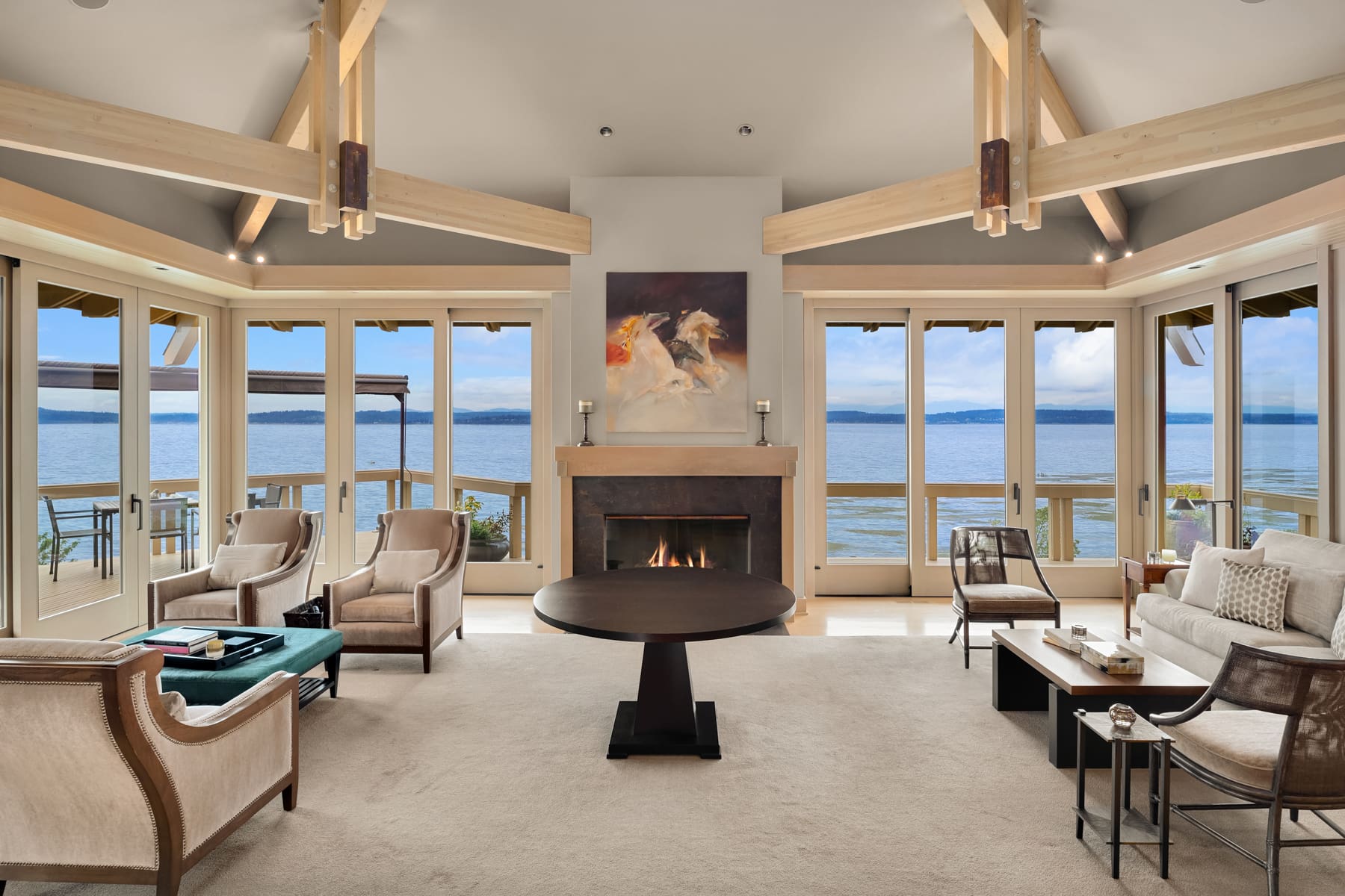 Spacious modern living room with panoramic water views, featuring elegant furnishings and a cozy fireplace, located in the Pacific Northwest.