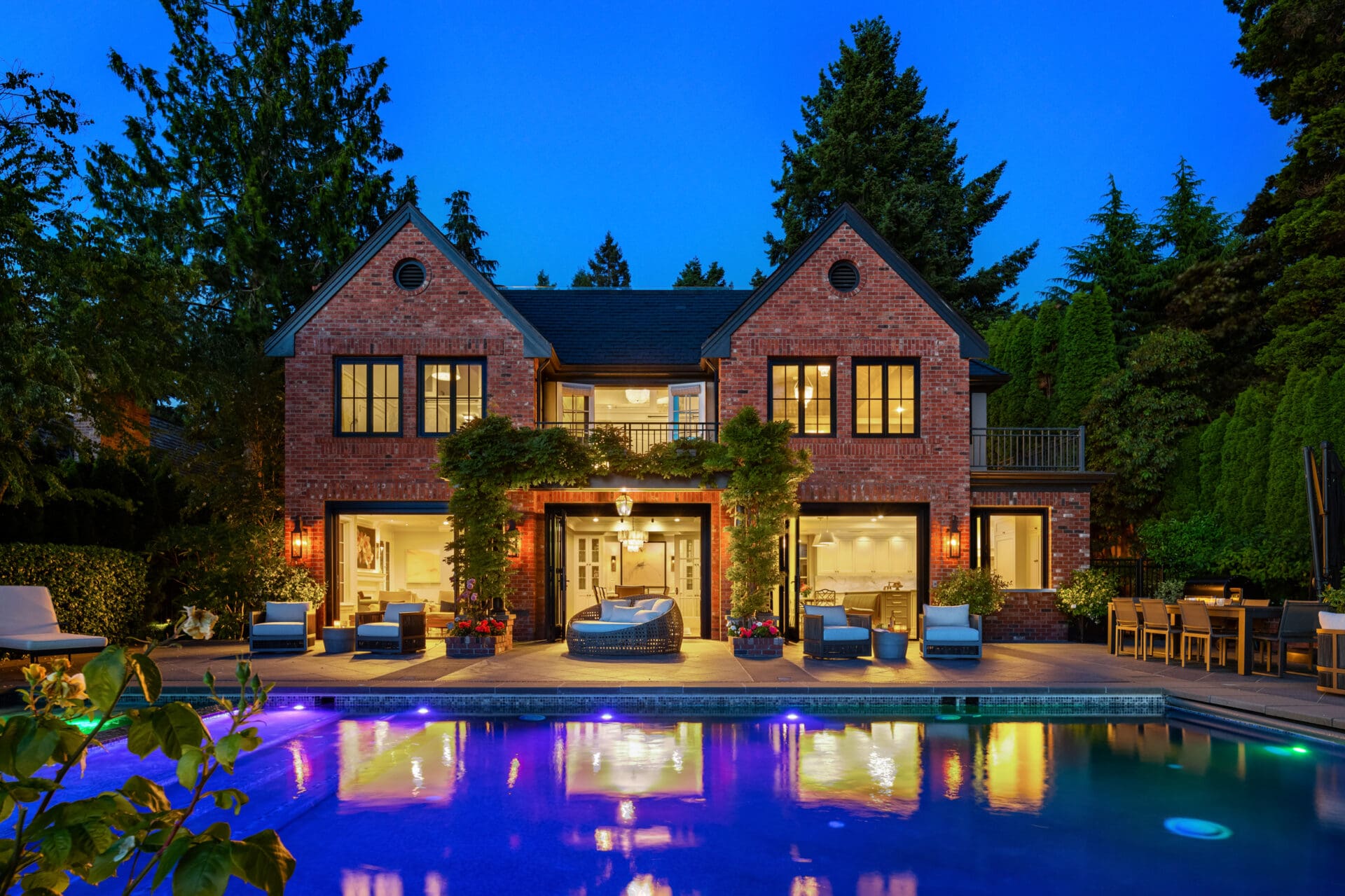 Elegant exterior view of a modern brick home with lush landscaping and a sparkling pool, illuminated at twilight in the Pacific Northwest.