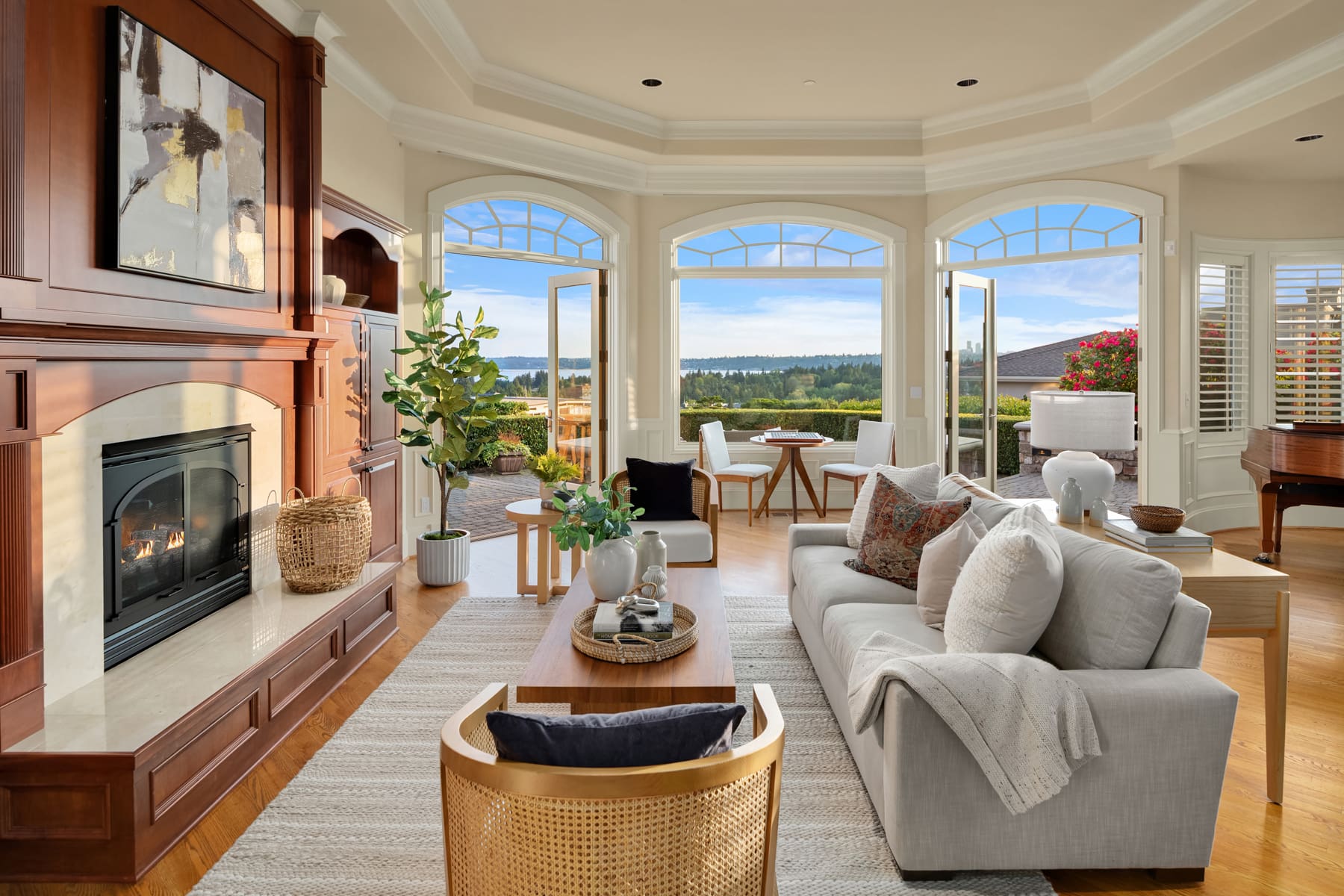 Elegant living room with large bay windows offering stunning views of the Pacific Northwest landscape, featuring a cozy fireplace, modern furnishings, and warm wood accents. Perfect for relaxing or entertaining.