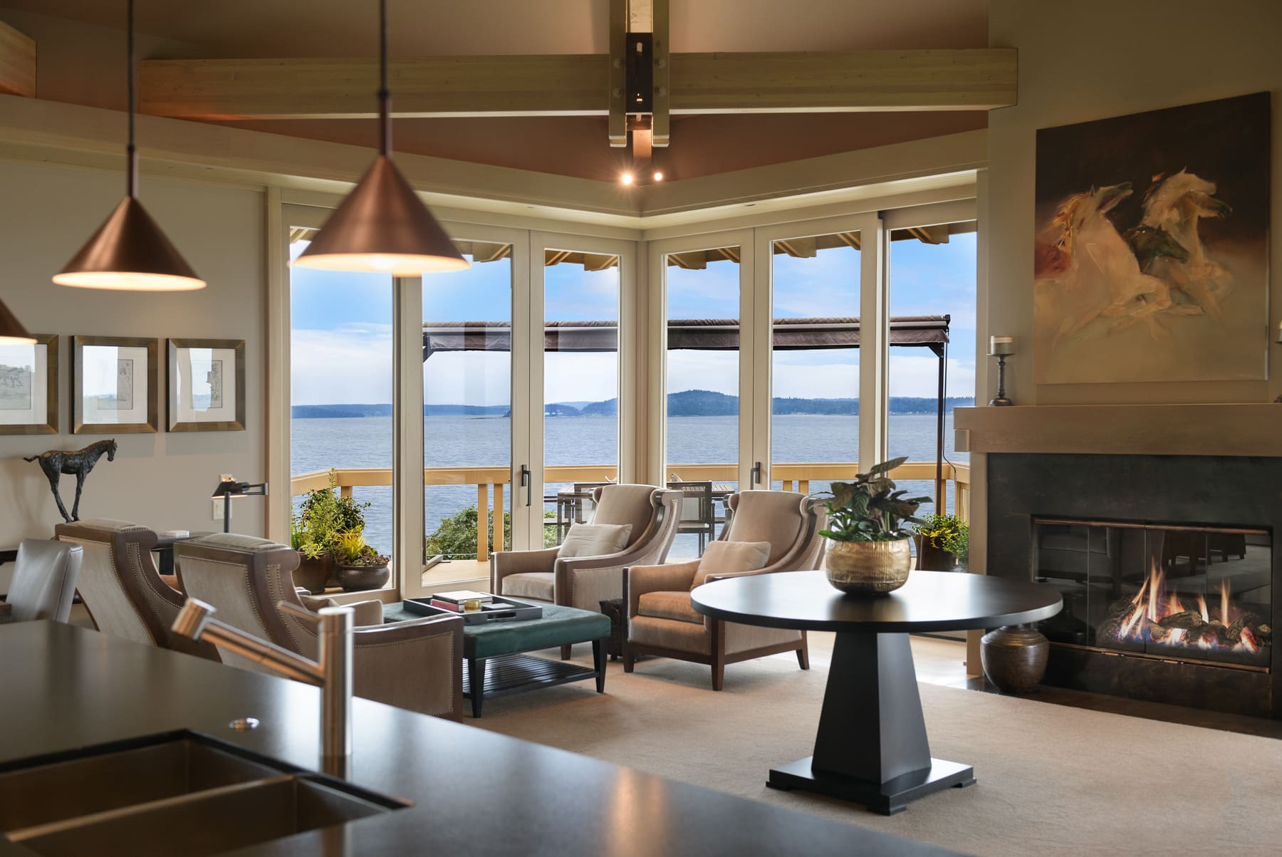 Elegant waterfront living room with modern design features, large windows offering stunning views of the water and mountains, cozy seating, and a fireplace, located in the Pacific Northwest.