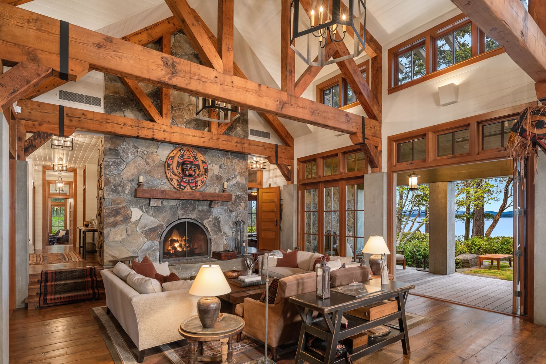 Spacious living room with rustic wooden beams and a stone fireplace, featuring elegant furnishings and large windows that showcase a scenic view of the outdoors, located in the Pacific Northwest.