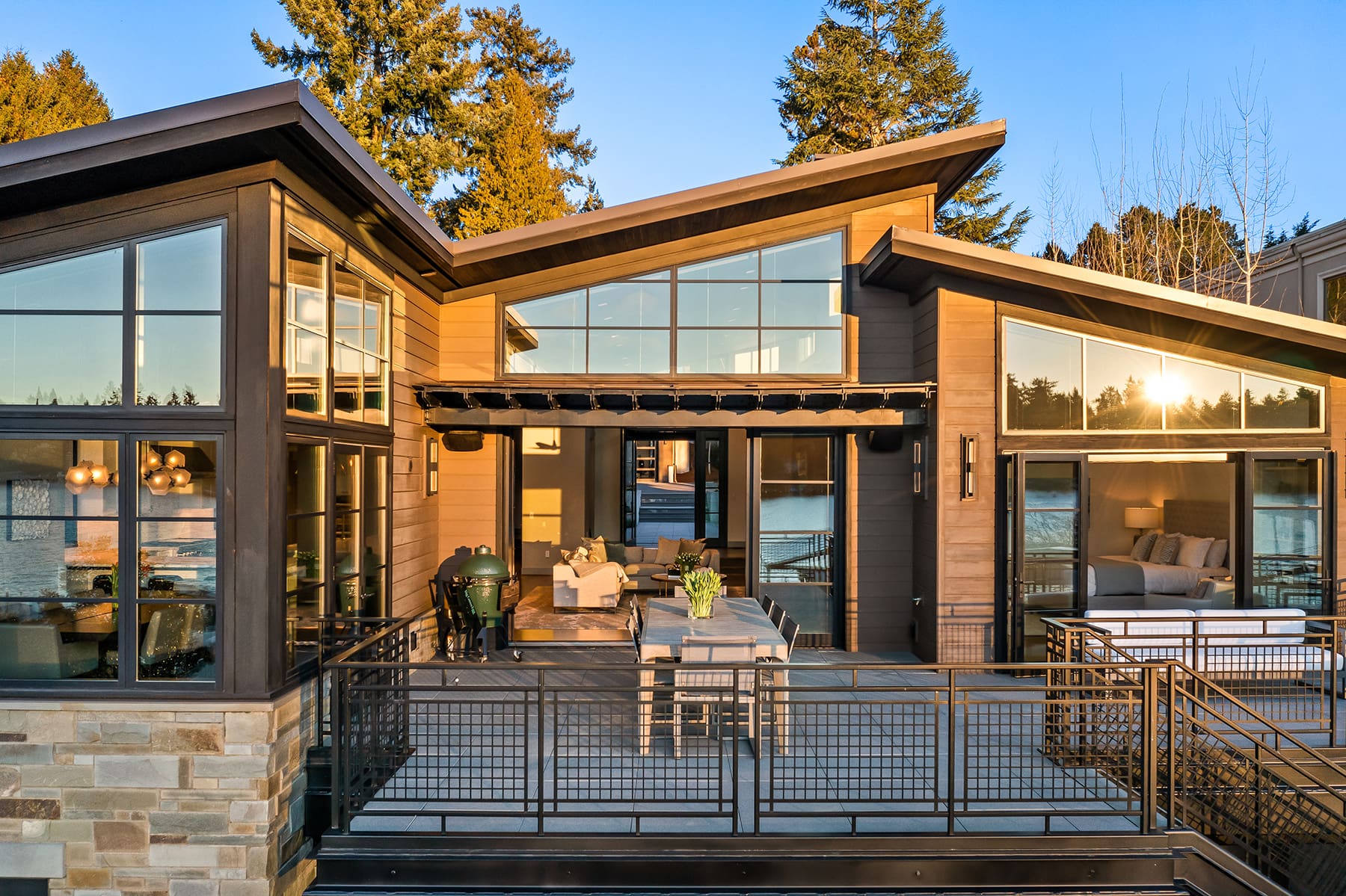 Modern waterfront home exterior with large windows and a spacious deck, featuring stylish outdoor seating and a grill, set in the scenic Pacific Northwest.