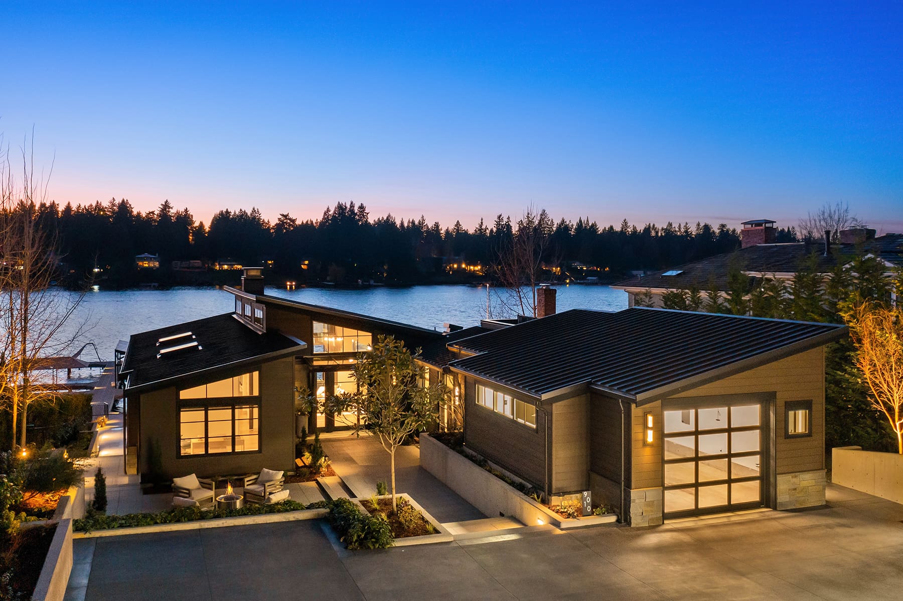 Modern waterfront home exterior at twilight in the Pacific Northwest, featuring sleek lines, large windows, and landscaped surroundings with a serene lake view.