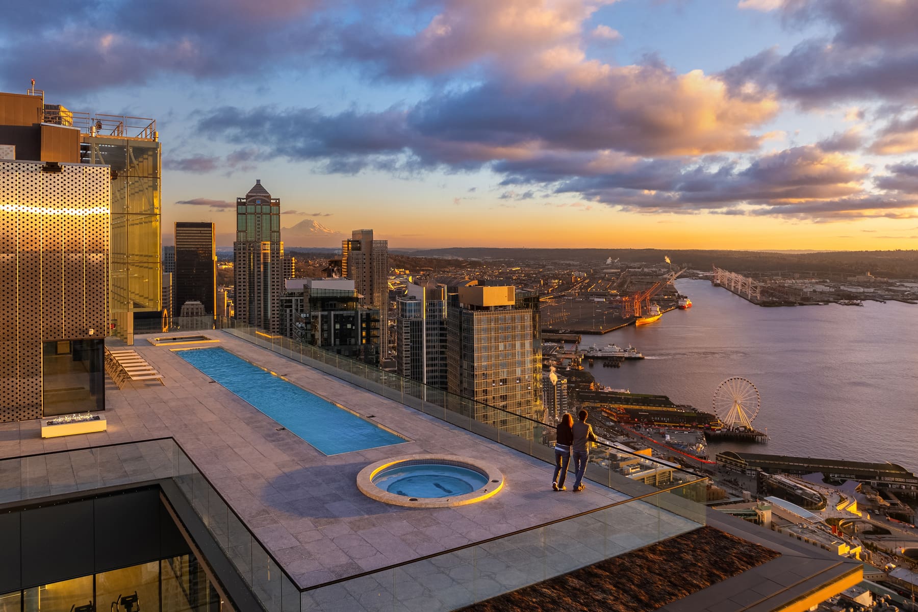 Rooftop pool and hot tub with stunning sunset views over Seattle's skyline and waterfront, showcasing a modern design and luxurious atmosphere.