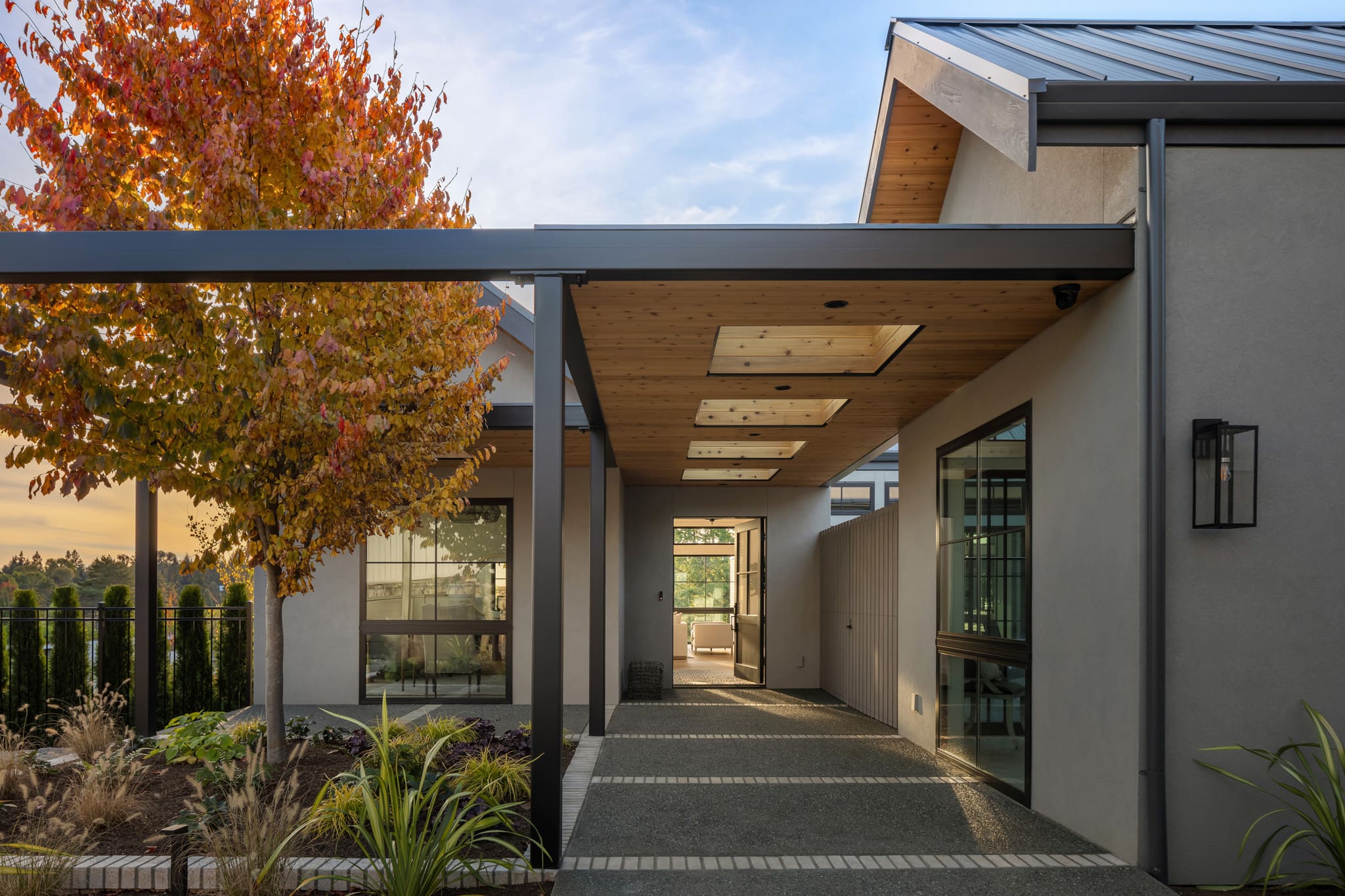 Modern exterior entrance of a contemporary home in the Pacific Northwest, featuring a stylish covered walkway, autumn foliage, and sleek landscaping elements.