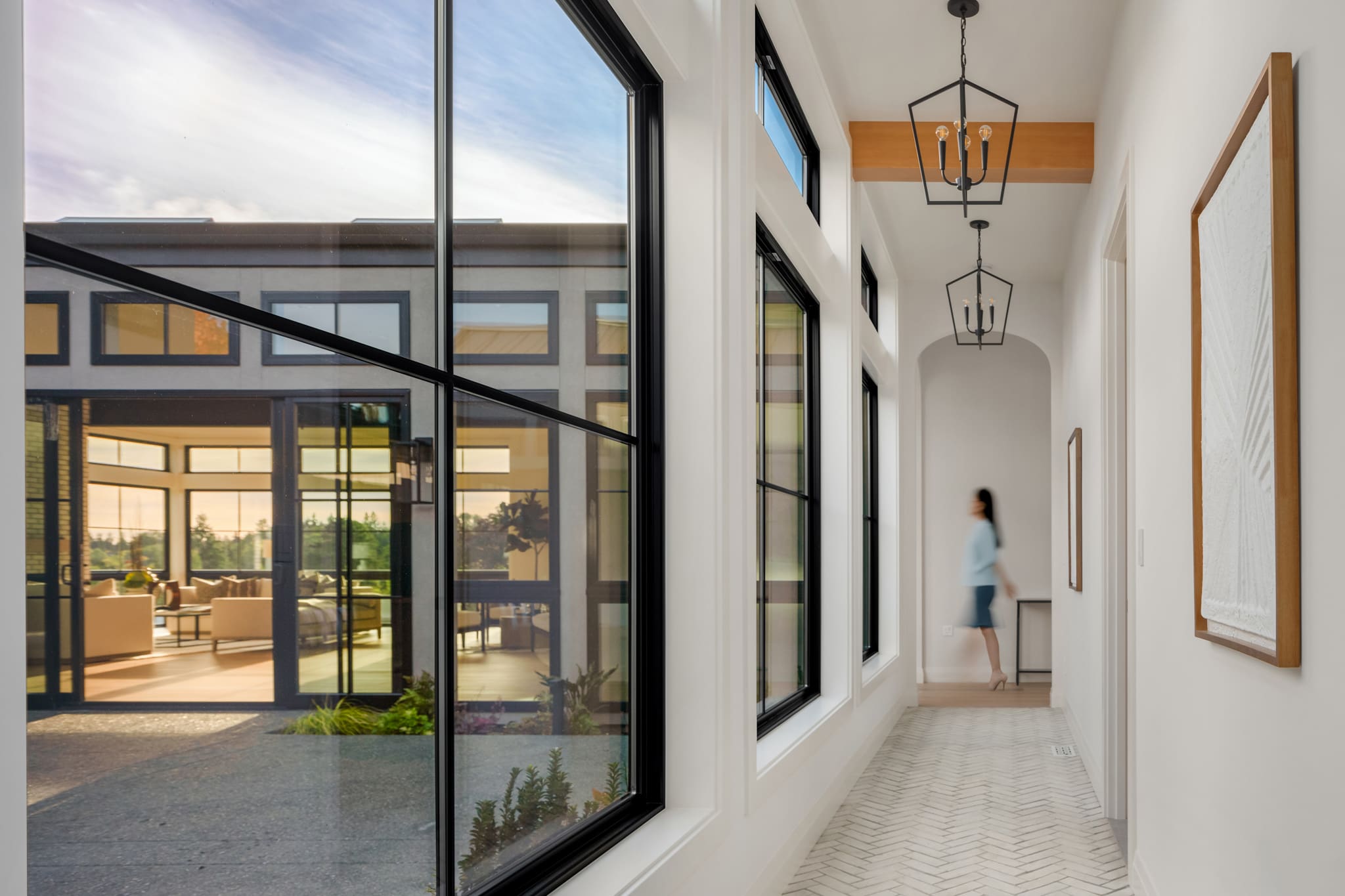 Bright and modern hallway featuring large black-framed windows, elegant light fixtures, and herringbone flooring, showcasing a view of a stylish living area in the Pacific Northwest.
