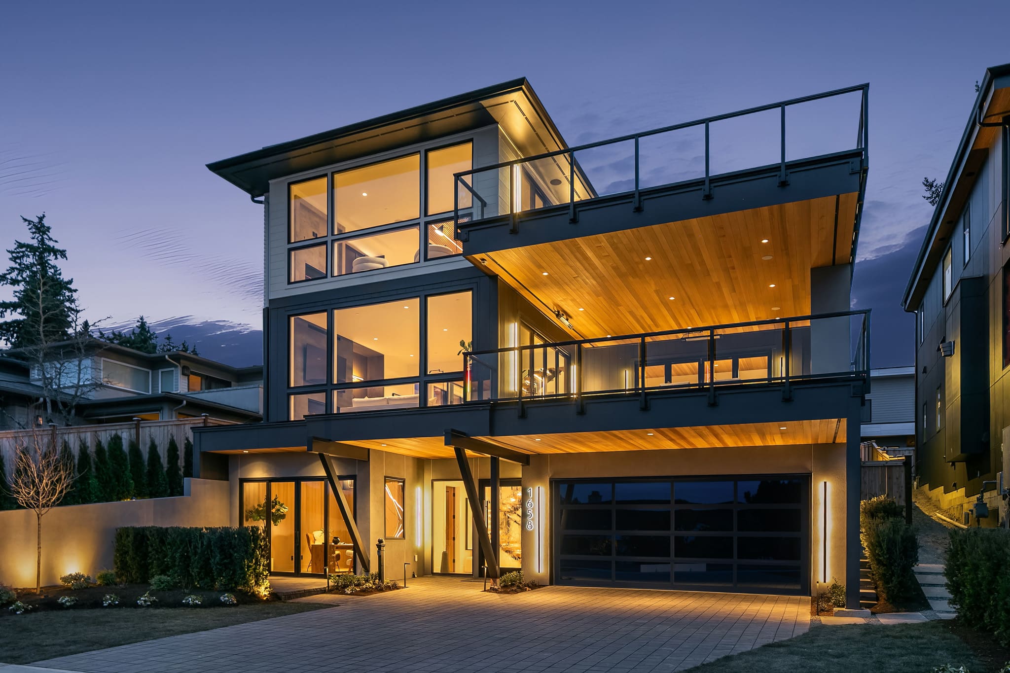 Modern exterior of a luxury home with expansive glass windows and wooden accents, illuminated at twilight in the Pacific Northwest.