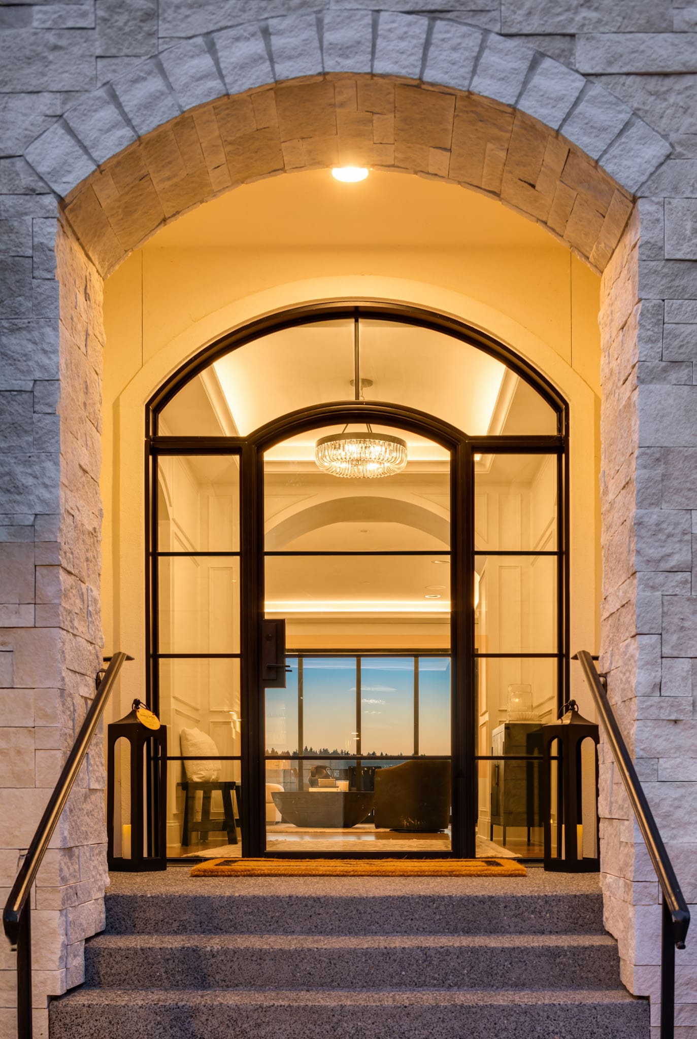 Elegant entrance of a modern home featuring a grand arched doorway and stylish chandelier, set against a twilight backdrop in the Pacific Northwest.