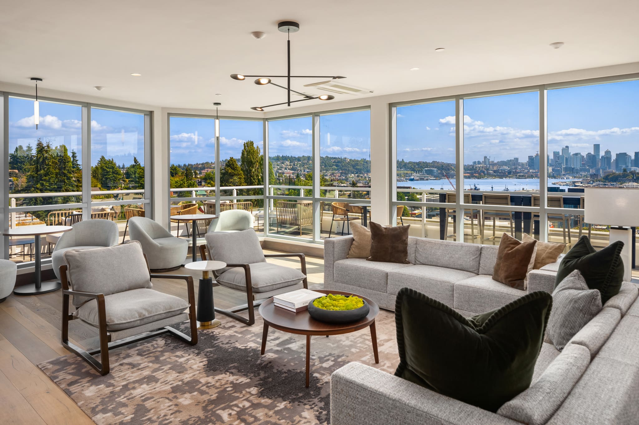 Modern living room with panoramic views of Seattle, featuring a stylish sectional sofa, elegant accent chairs, and a round coffee table, creating a bright and inviting atmosphere.
