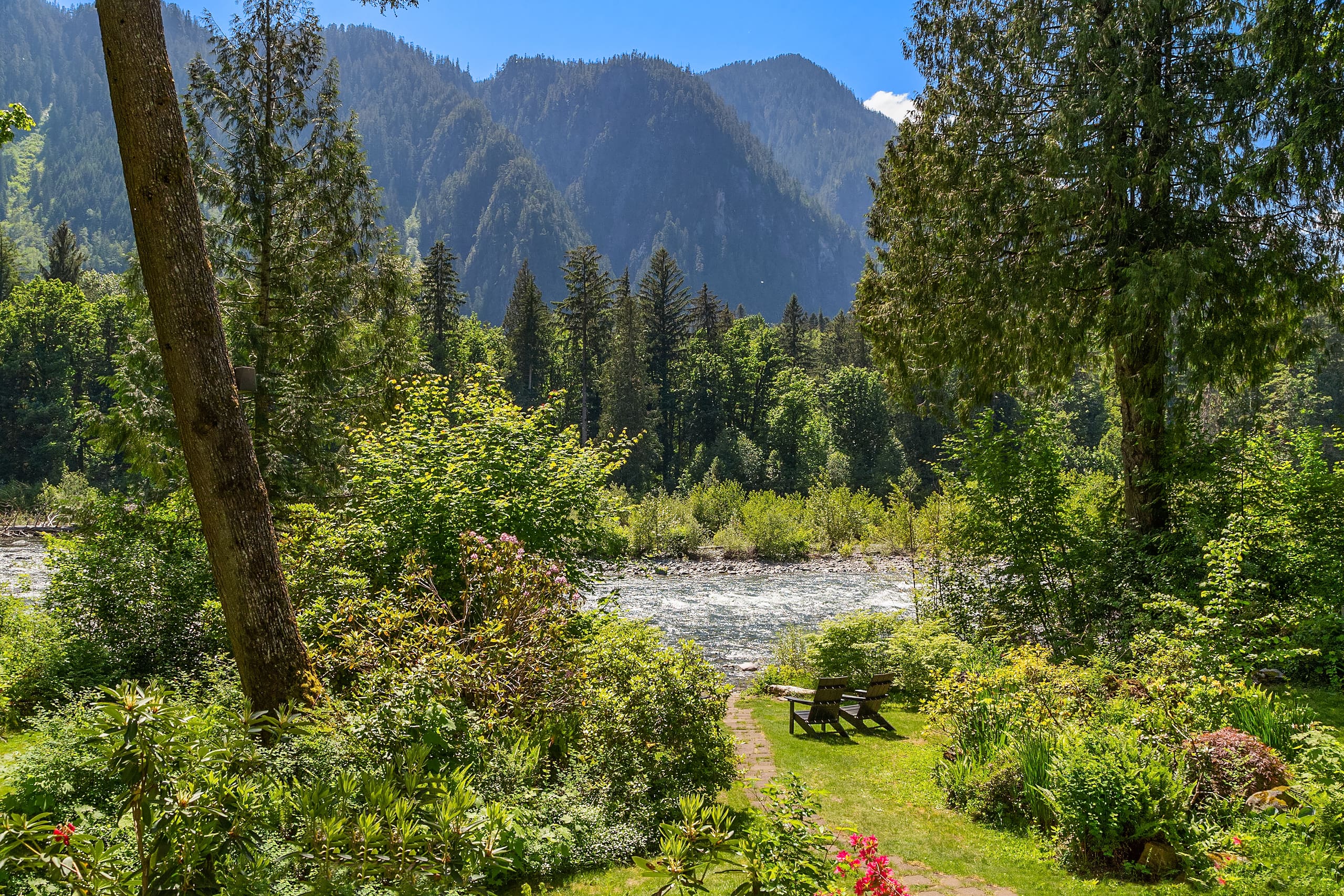 Scenic riverfront garden with lush greenery and mountains in the background, showcasing a tranquil outdoor space in the Pacific Northwest.