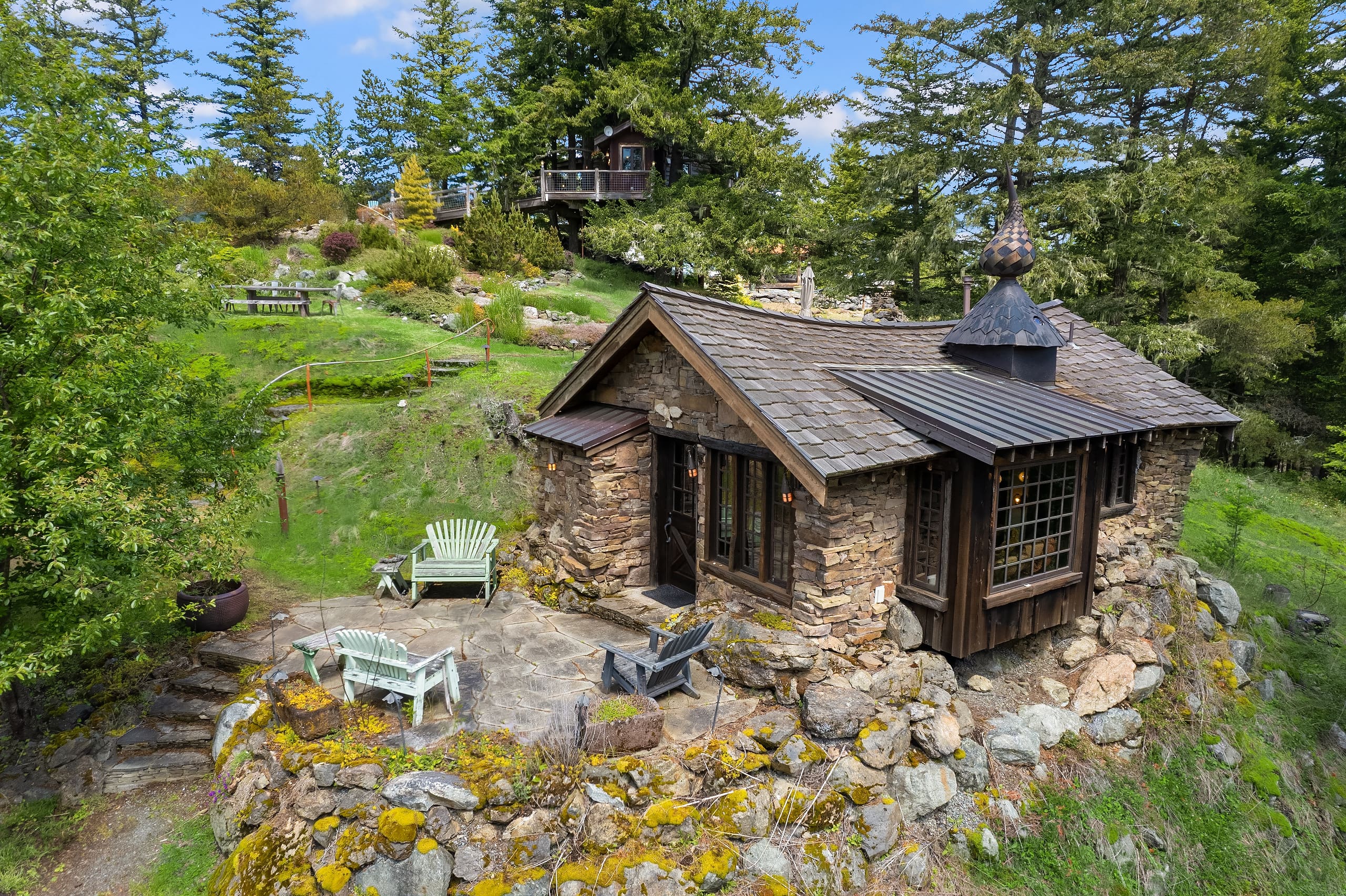 Charming stone cottage exterior surrounded by lush greenery and rocky landscape in the Pacific Northwest, featuring a cozy outdoor seating area and unique architectural details.